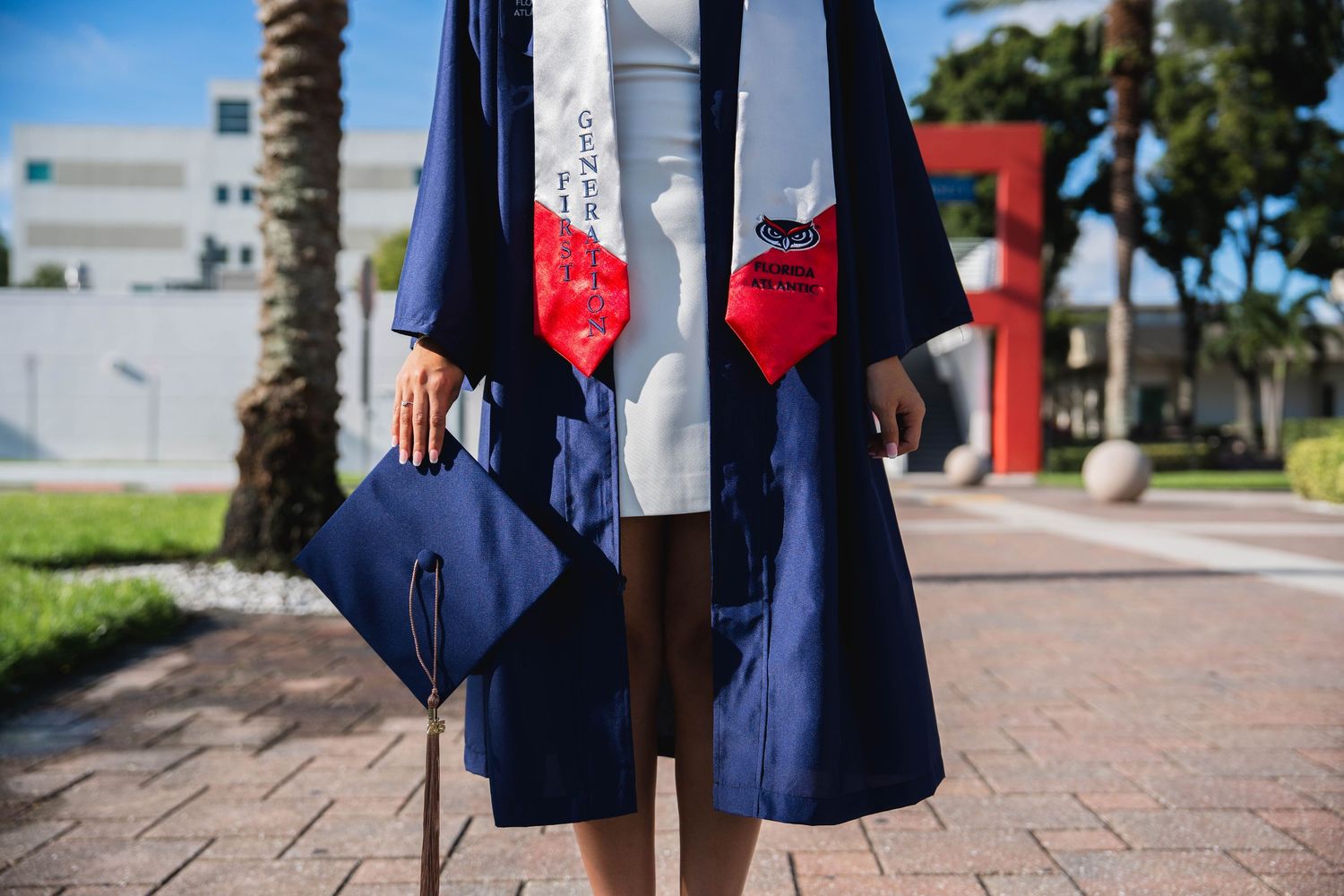 Detail photo of FAU student in graduation gown holding cap outdoors