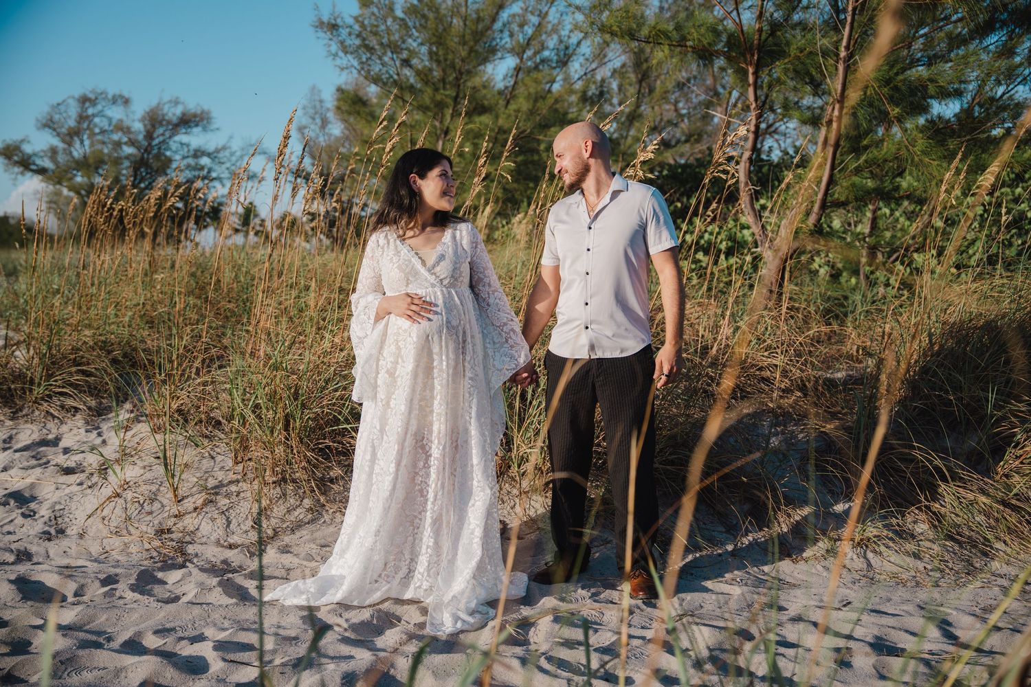 Couple walking hand in hand on sandy Dania Beach during maternity session