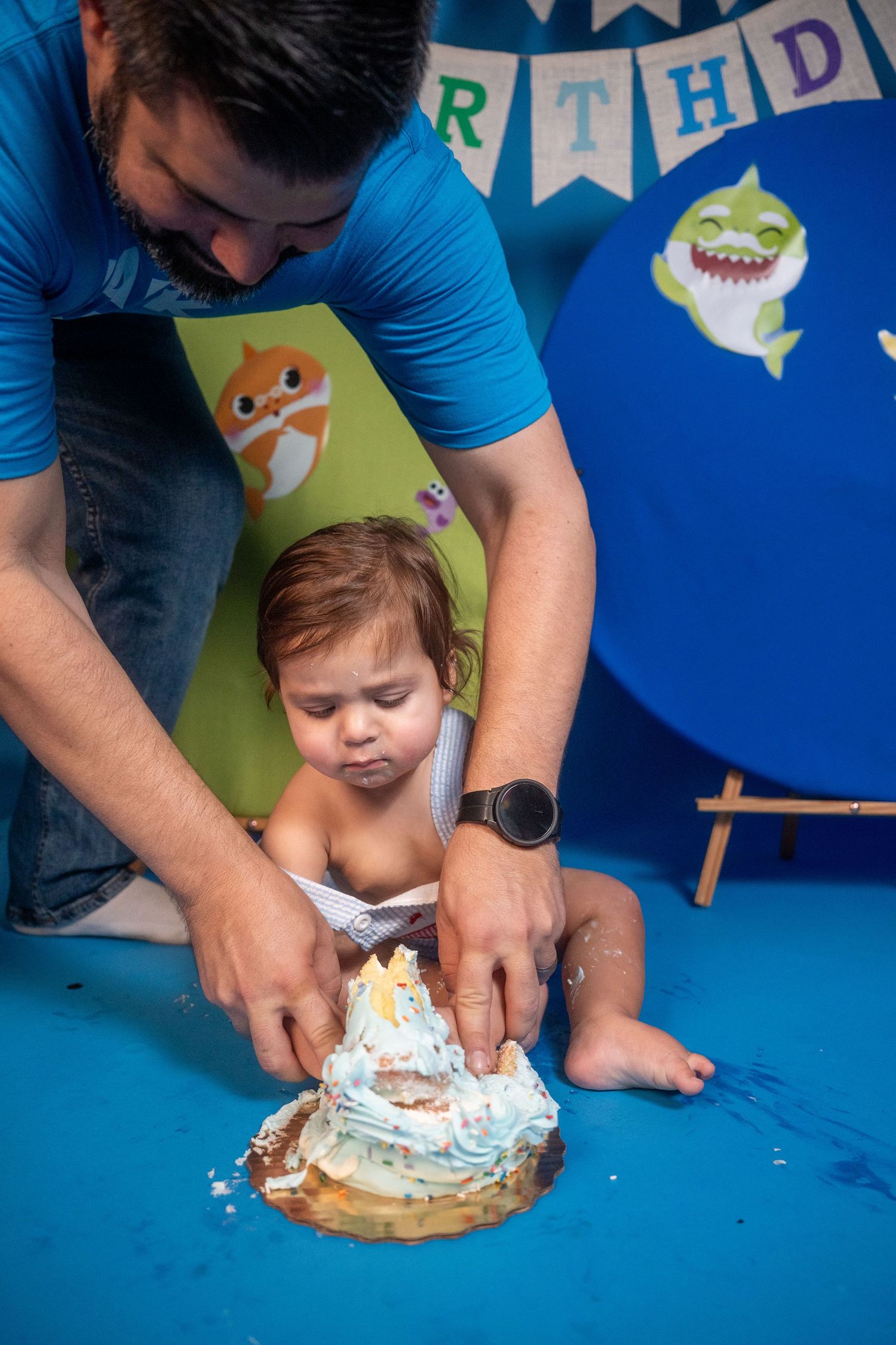 First birthday cake smash moment with a toddler assisted by a parent during a studio birthday session.