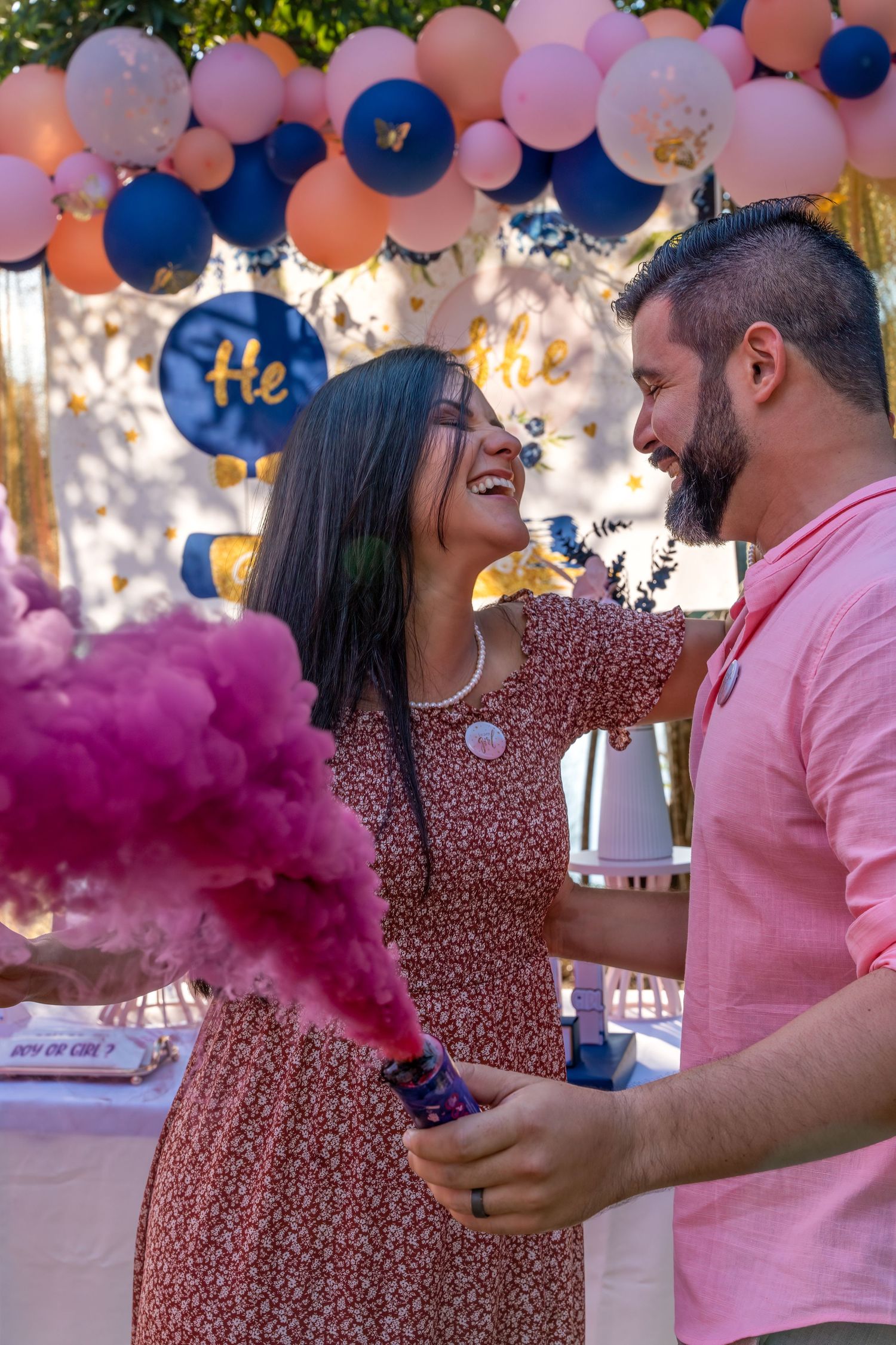 Expecting couple facing each other beneath a balloon arch with pink smoke during a South Florida gender reveal.
