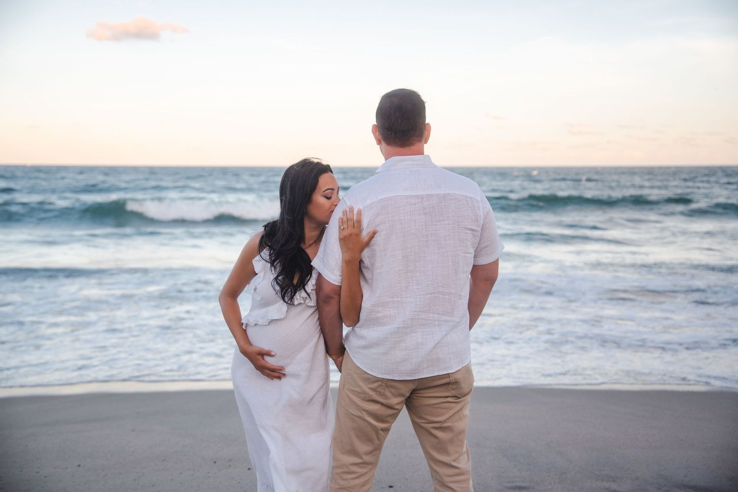 Beachside pregnancy announcement portrait of an expecting couple standing together by the ocean, photographed at sunset in Deerfield Beach,