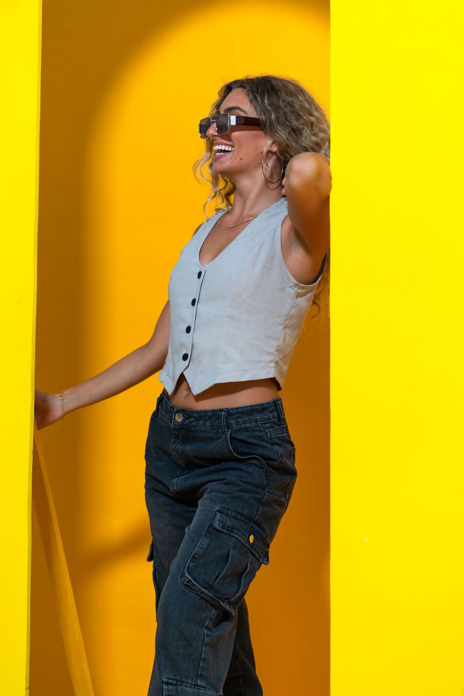 Vibrant fashion shoot at HGAB Studios – woman in cargo pants and a crop top strikes a pose in front of a sunlit yellow wall.