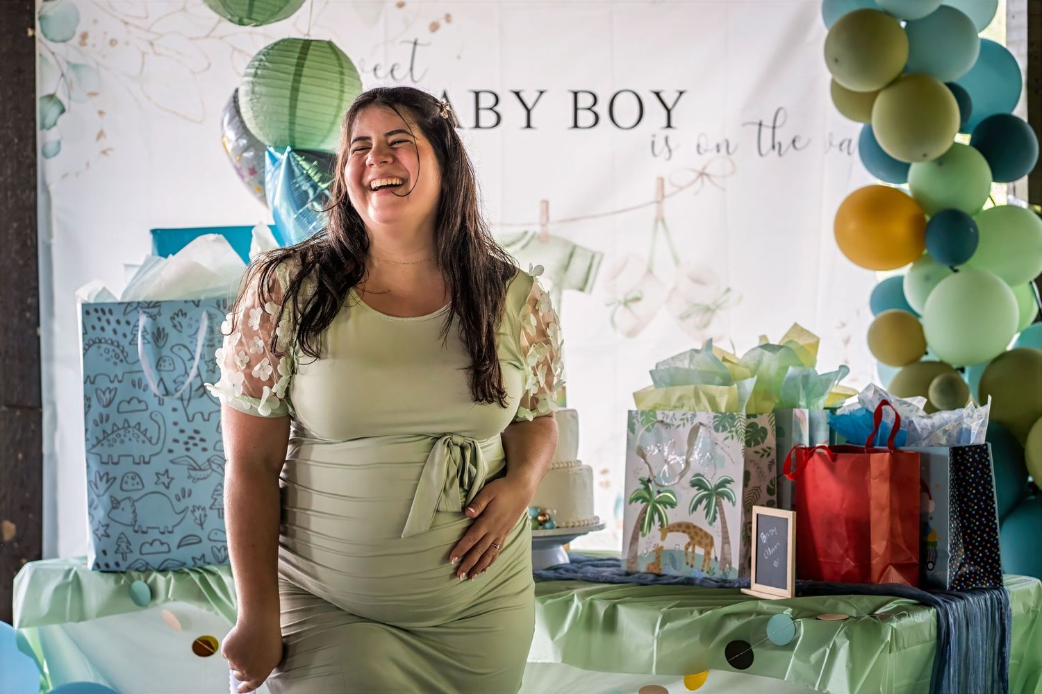Expecting mother smiling in front of baby shower decorations during a South Florida celebration.