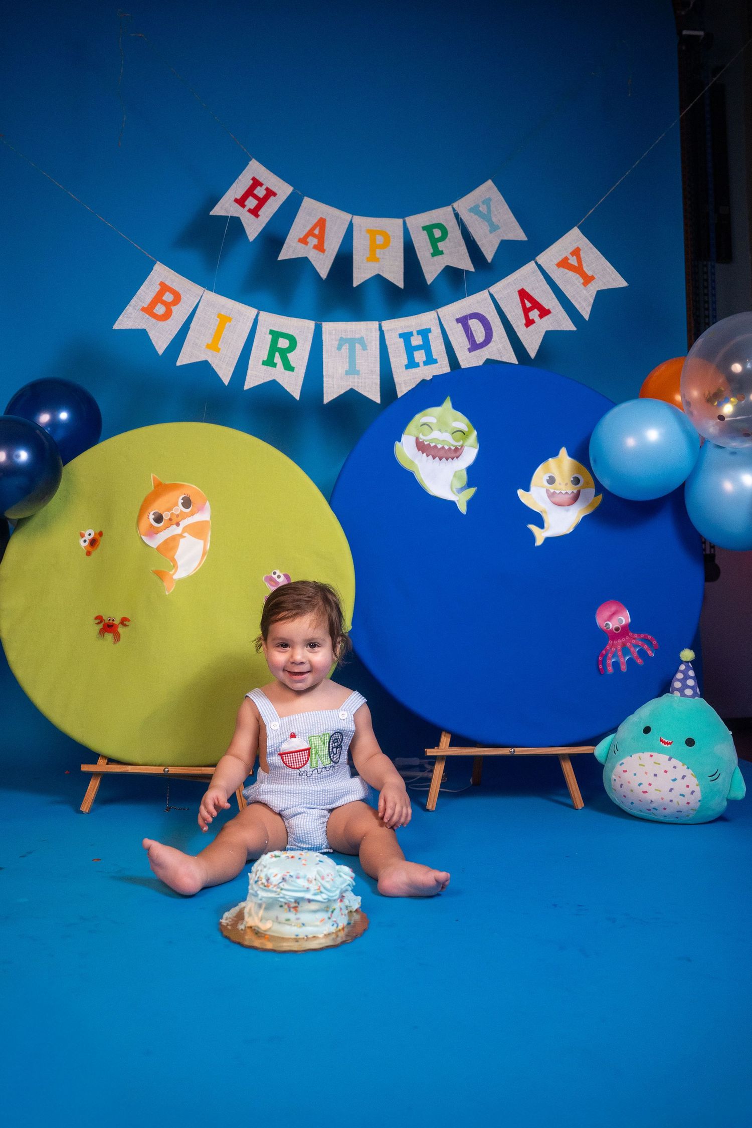 Toddler seated alone during a first birthday cake smash session with playful decorations.