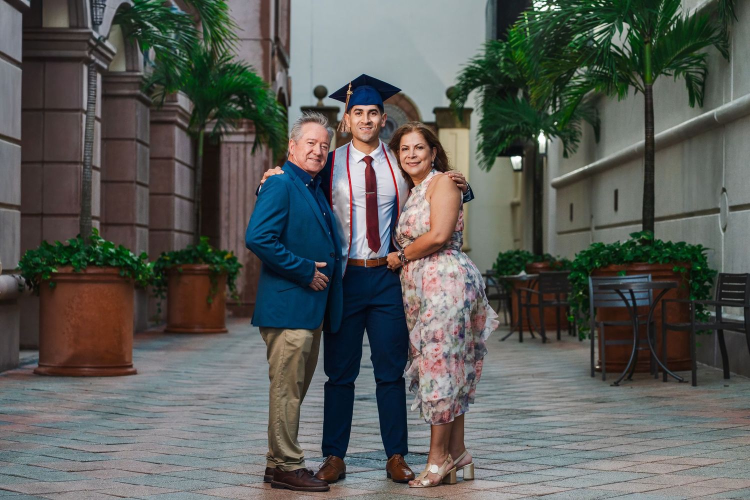 Florida Atlantic University graduation portrait of a graduate standing with parents in a palm-lined courtyard.
