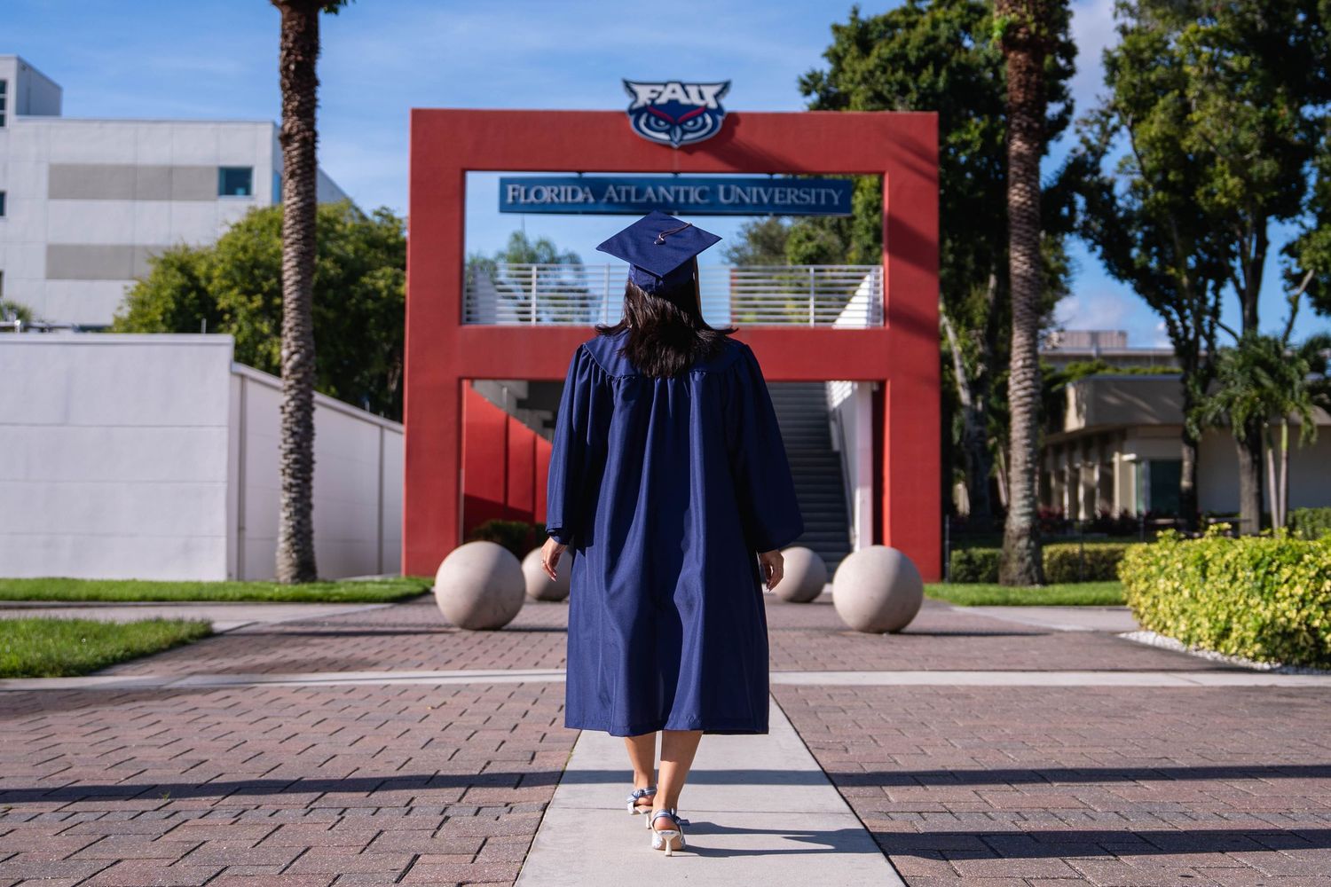 South Florida graduation photo of FAU student walking toward university sign in gown
