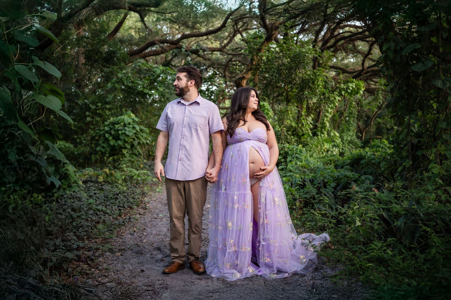 A couple stands together on a forest path wearing coordinated lavender and brown outfits during a romantic photoshoot.Hollywood Photographer