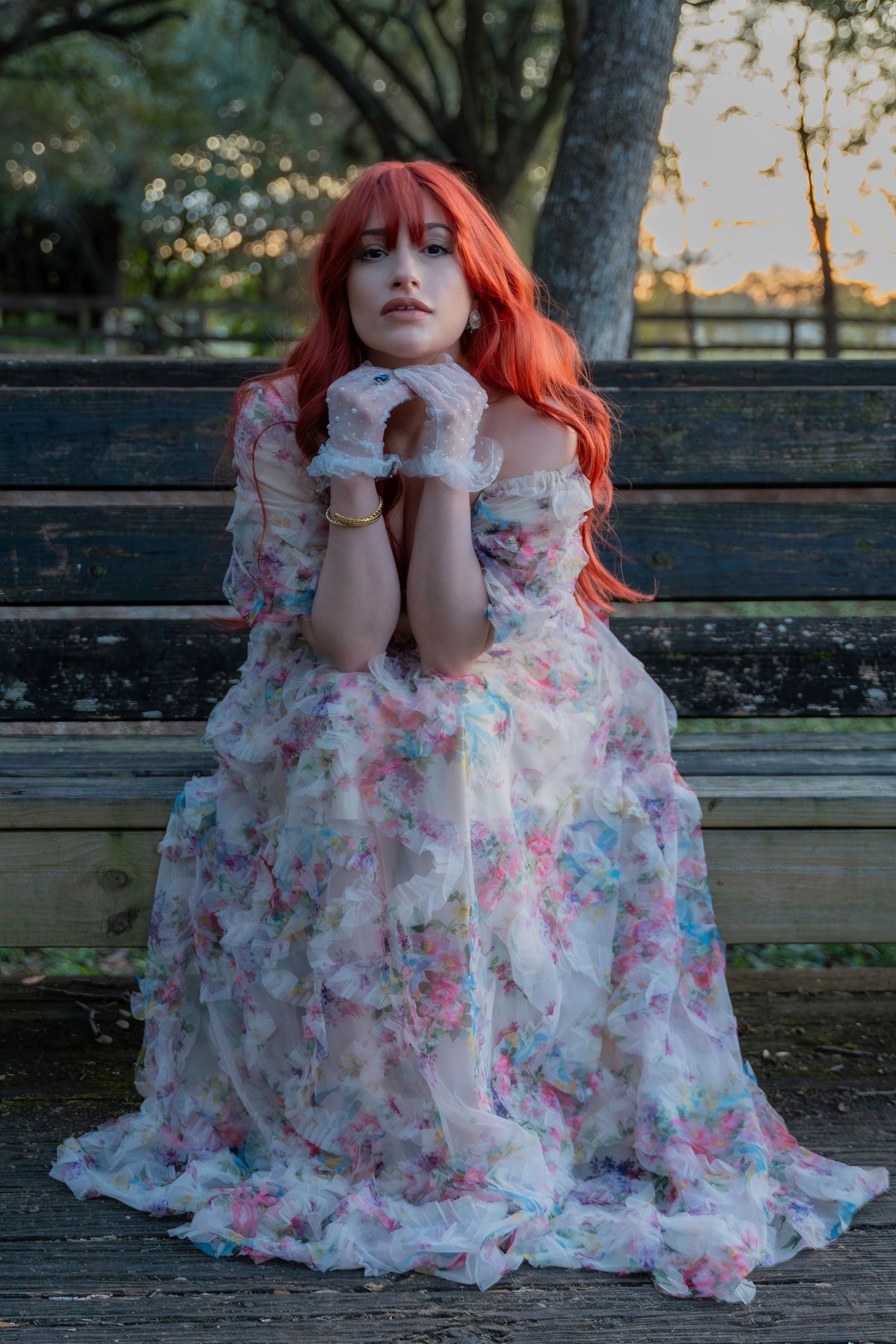 Romantic vintage aesthetic – red-haired woman in a ruffled floral gown gazes into the distance on a park bench at sunset Amelia Earhart Park