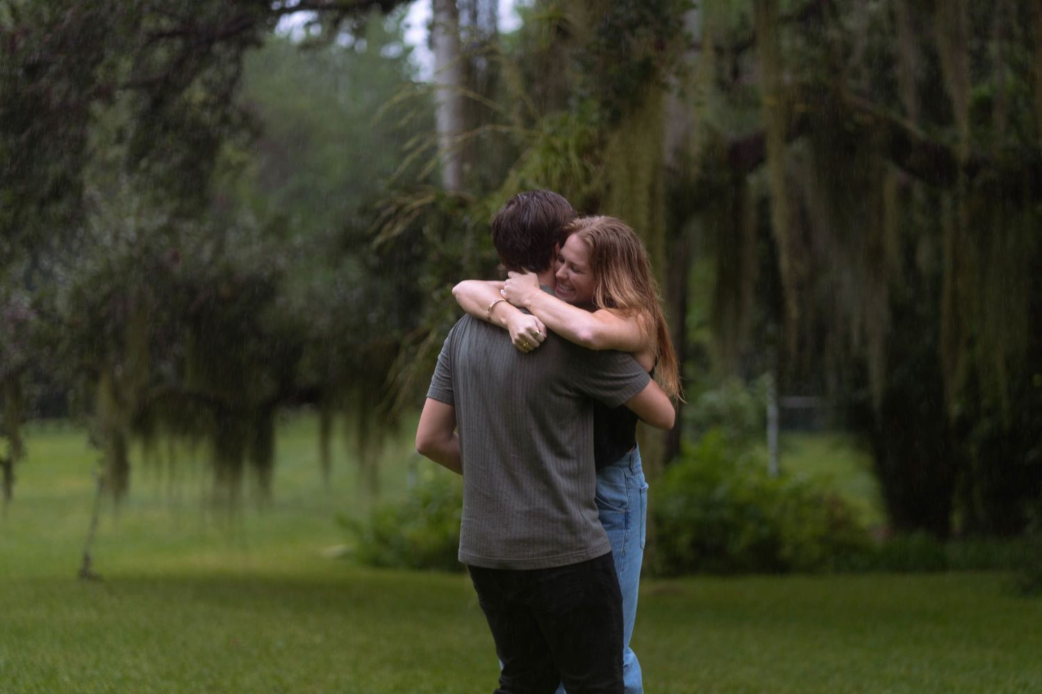 Engaged couple shares a heartfelt hug surrounded by tropical trees at The Kampong, a scenic Miami botanical garden.