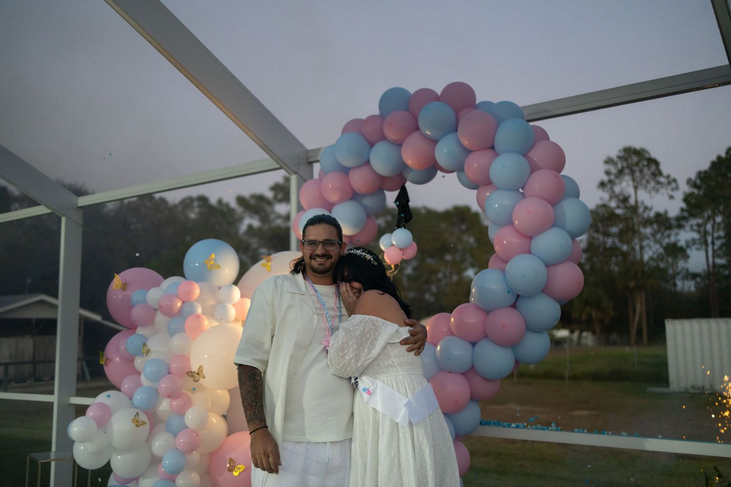Expecting couple posing together beneath a pink and blue balloon arch during a South Florida gender reveal party.