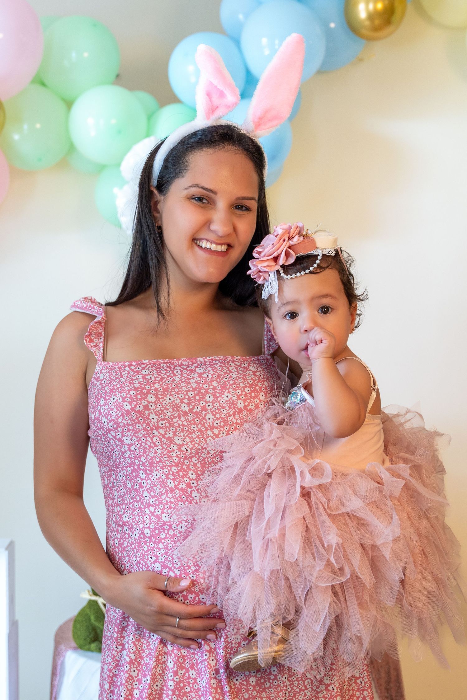 Mother holding her baby daughter in a pink dress and bunny ears during a first birthday portrait session.