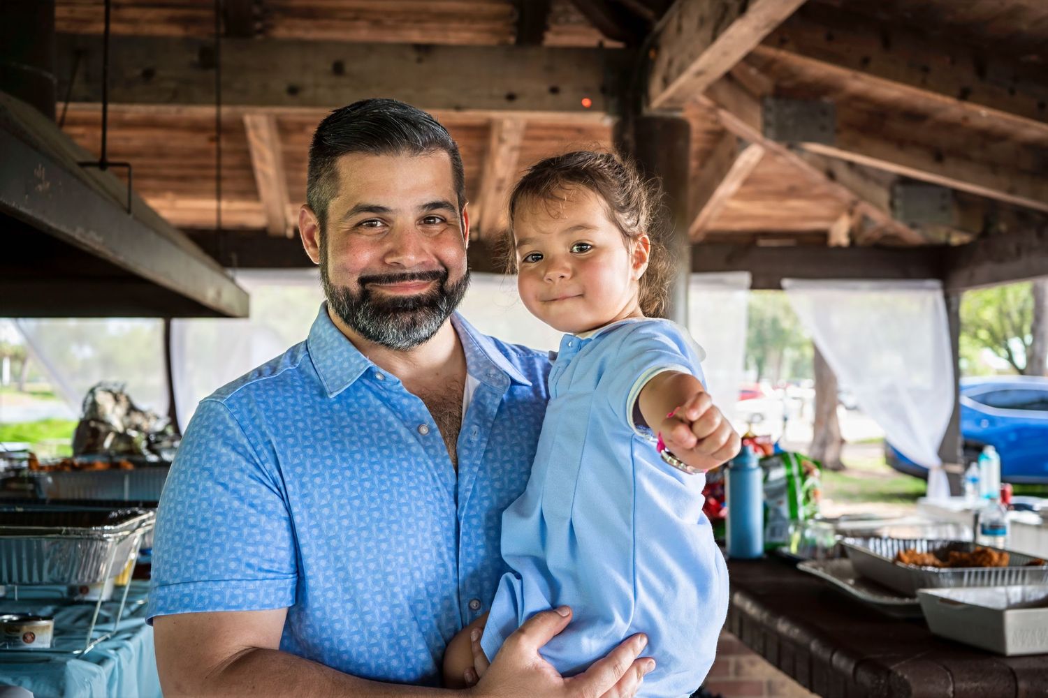 Father holding his young child and smiling during a relaxed outdoor baby shower gathering in South Florida.