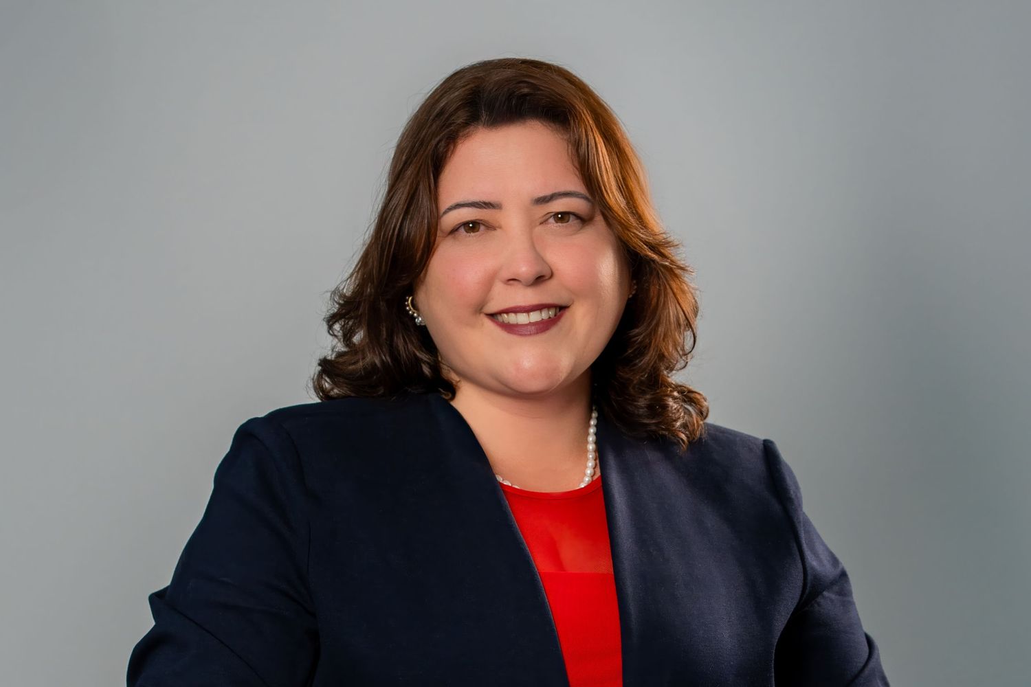 Friendly studio headshot of a professional woman CEO in a red top and navy blazer.