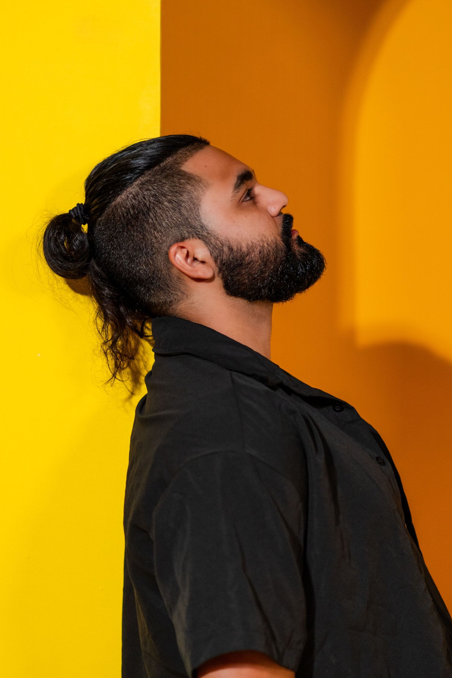 Bold fashion portrait in Wynwood, Miami – male model in black poses against a vibrant yellow and orange arched background.