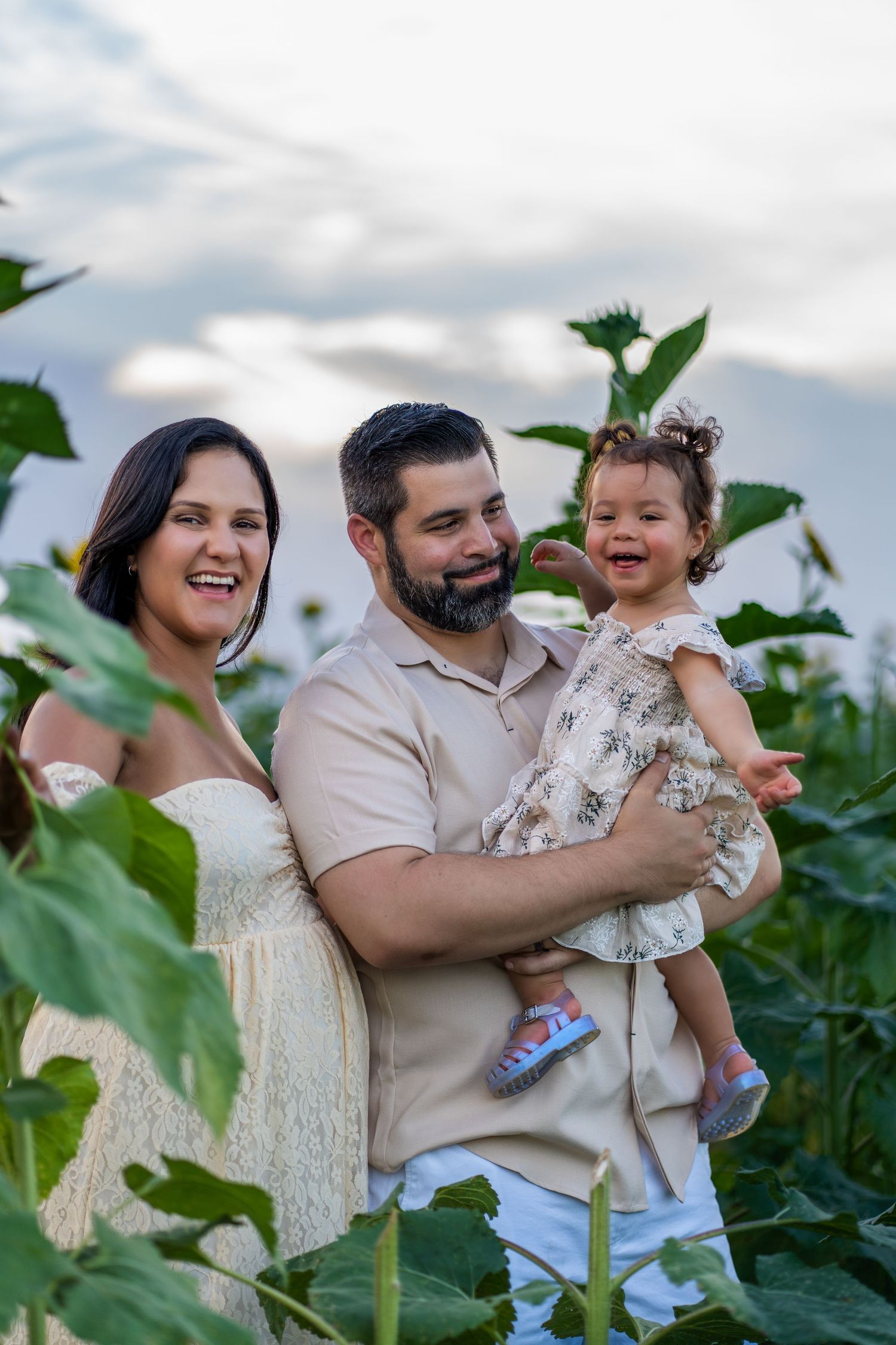 Heartwarming family maternity session in Homestead, capturing parents and their little one in a field of sunflowers.