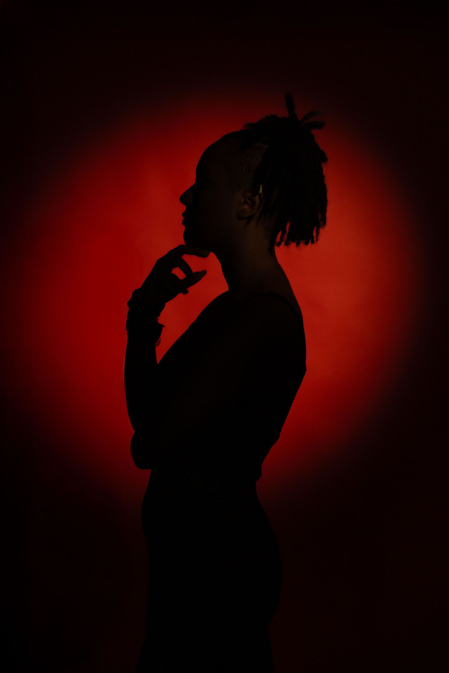 Artistic senior silhouette portrait captured in studio lighting against a red backdrop for a dramatic, cinematic look.