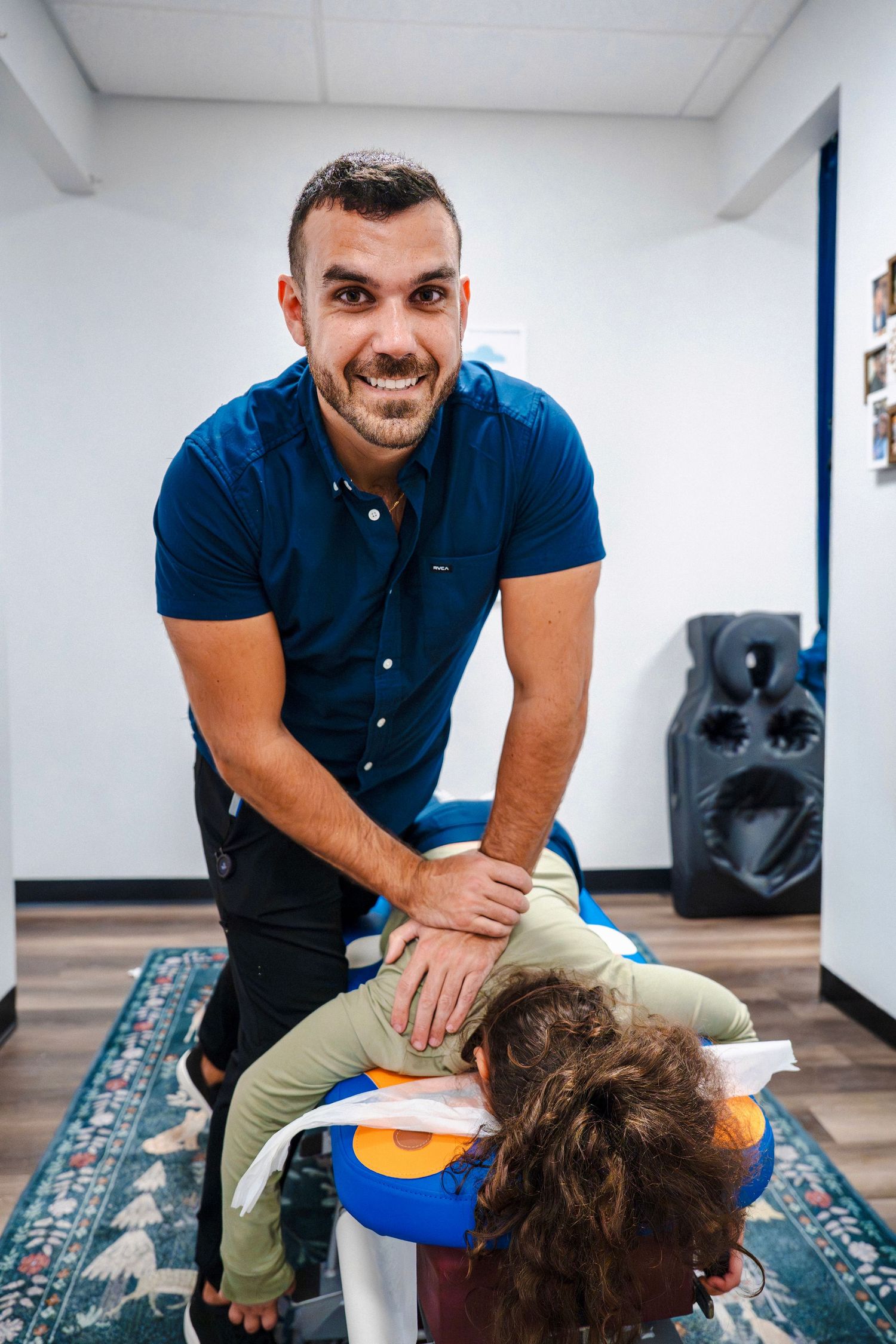 Chiropractor performing upper back adjustment on patient inside modern treatment room during clinic branding session