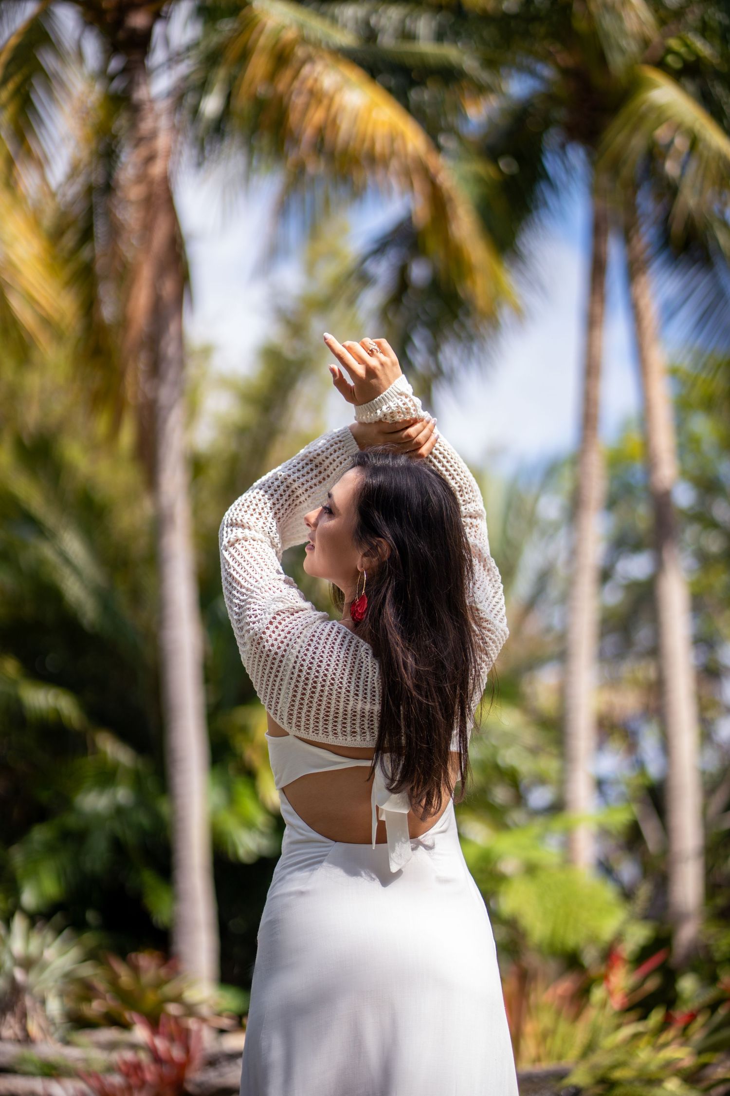 Portrait of woman in white dress standing with back turned in tropical botanical garden