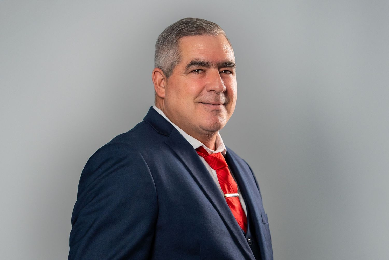 Man in navy suit posing for professional headshot on gray background
