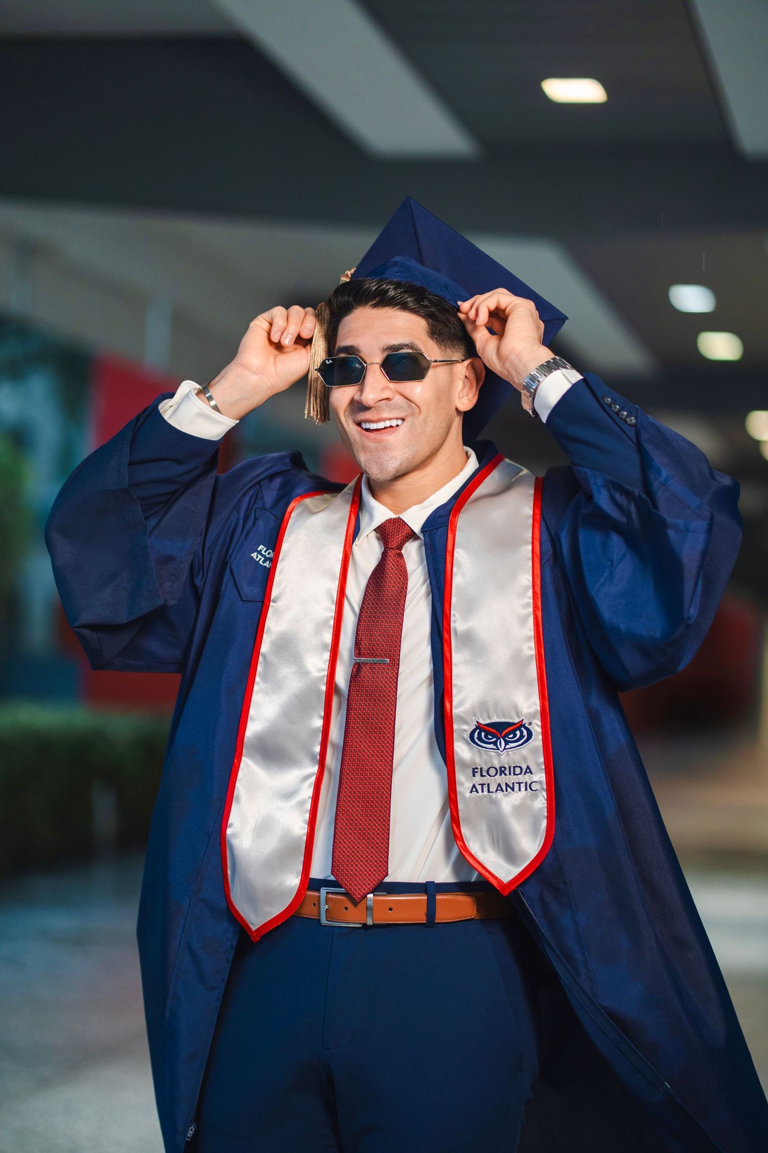 FAU graduation portrait of a graduate adjusting their cap indoors, celebrating a college milestone in South Florida.