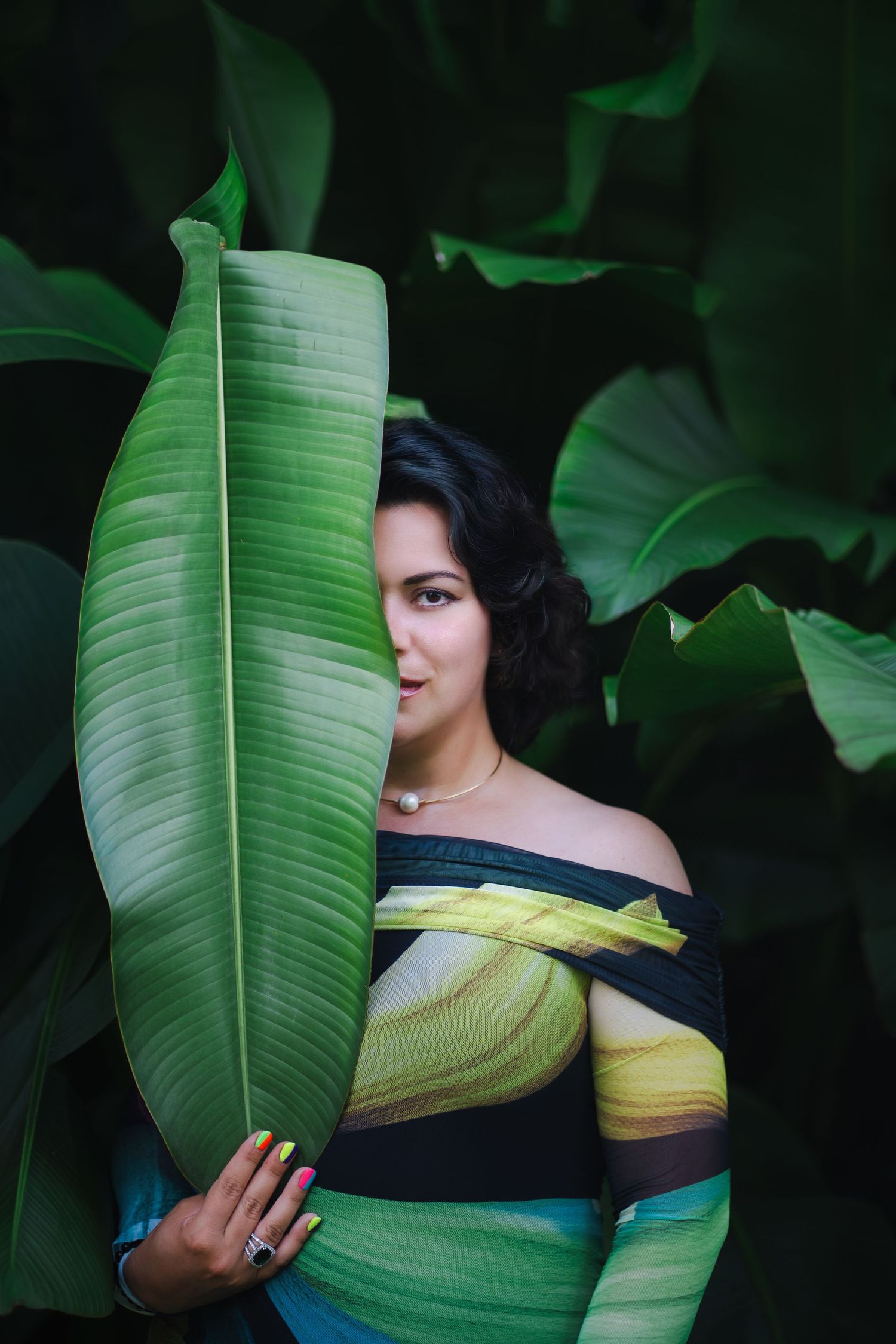 Creative branding portrait of a woman partially hidden behind tropical leaves at Fairchild Botanical Garden.