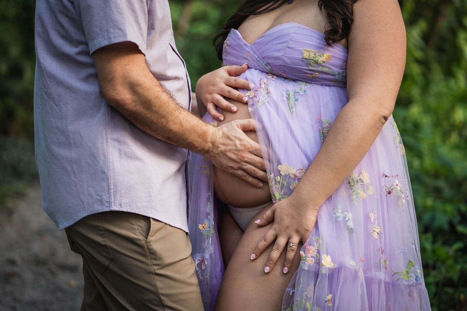 Close-up maternity portrait of an expecting couple holding their baby bump, captured outdoors with a natural, documentary-style approach.