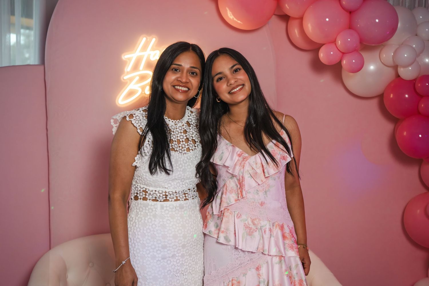 Mother and daughter in dresses smiling together at a birthday event with a pink party theme.