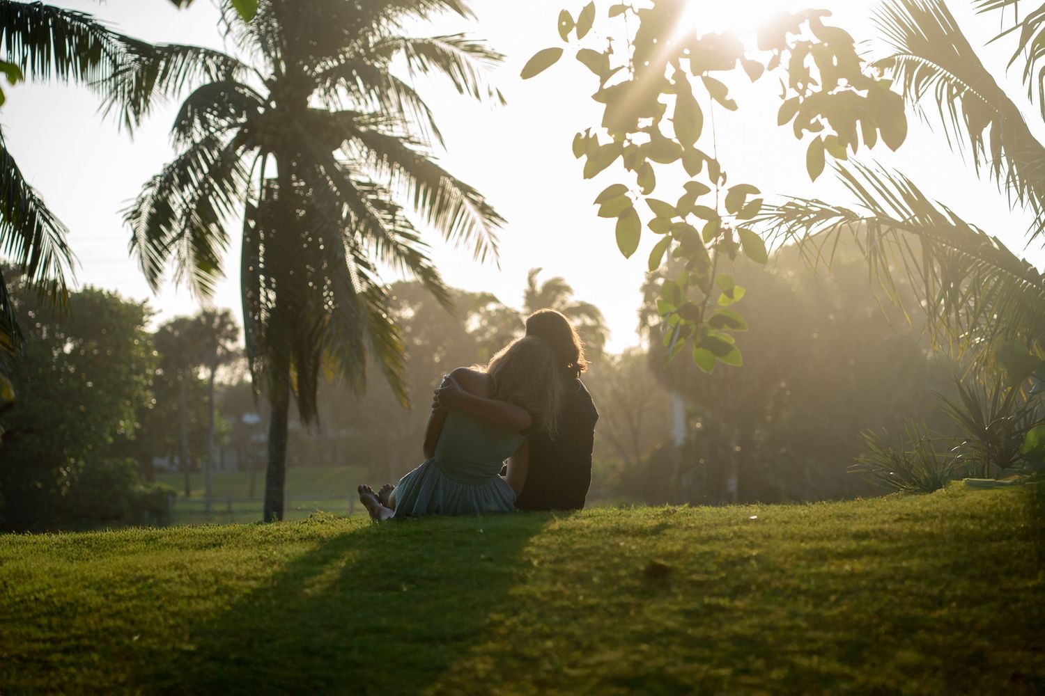 Couple sitting on grass at sunset under palm trees in South Florida engagement session