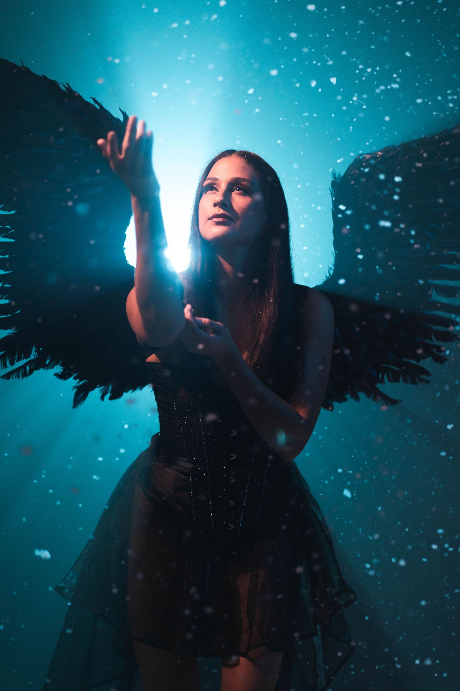 Ethereal dark angel concept at CFX Studio, Miami, FL – woman with black wings reaching towards glowing light.