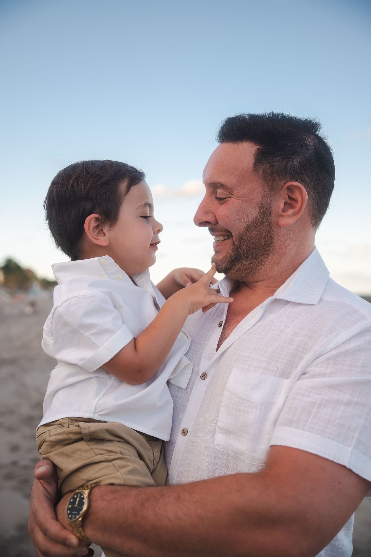 Father holding his young child during a pregnancy announcement photo session by the ocean.
