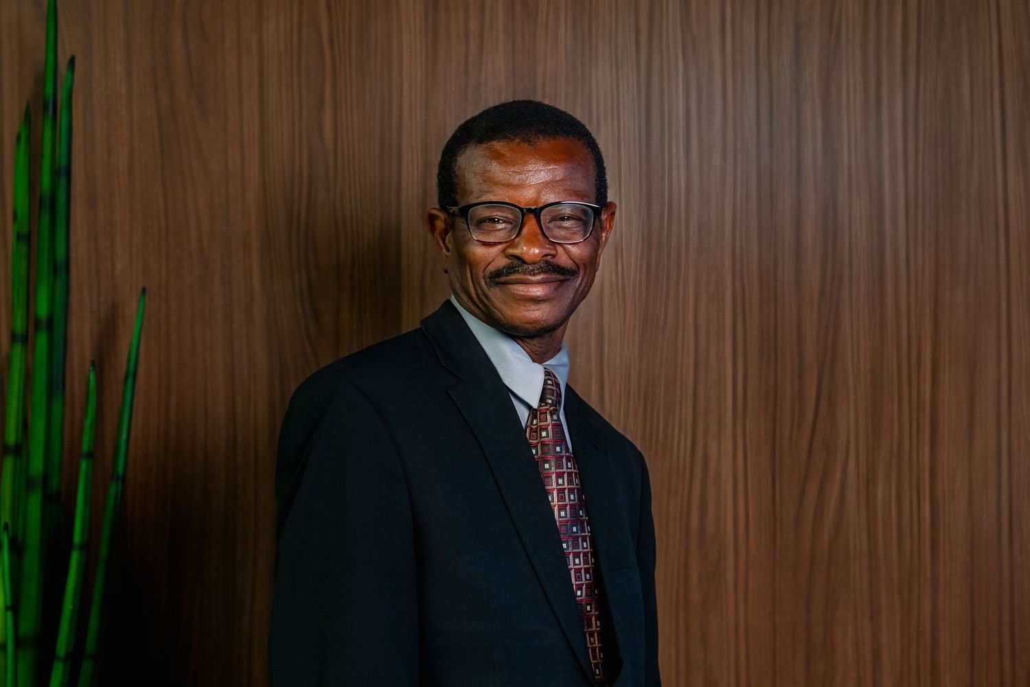 Businessman in suit smiling against wood-paneled background