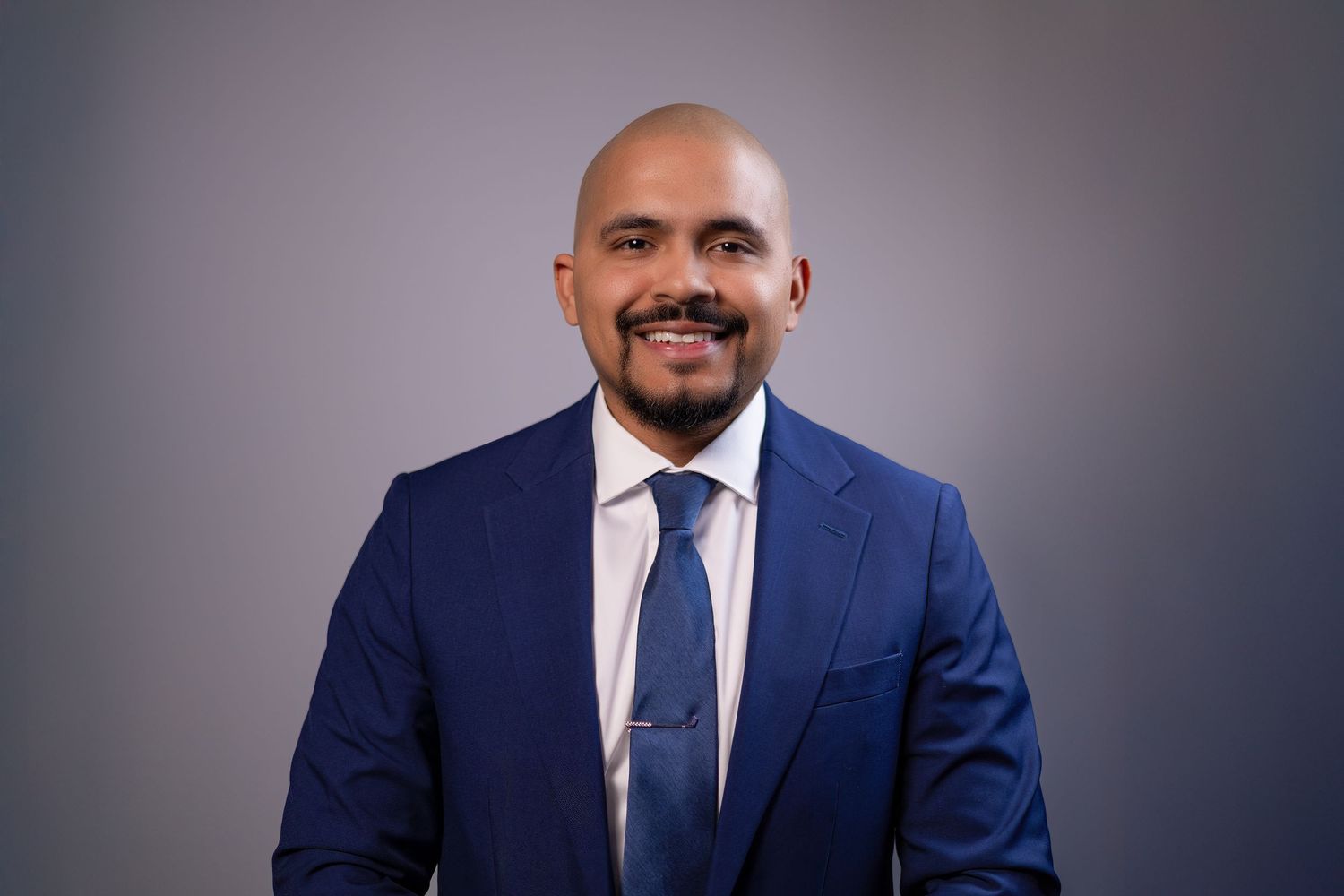 Smiling man in a dark blue suit jacket taken during a clean, corporate-style headshot.