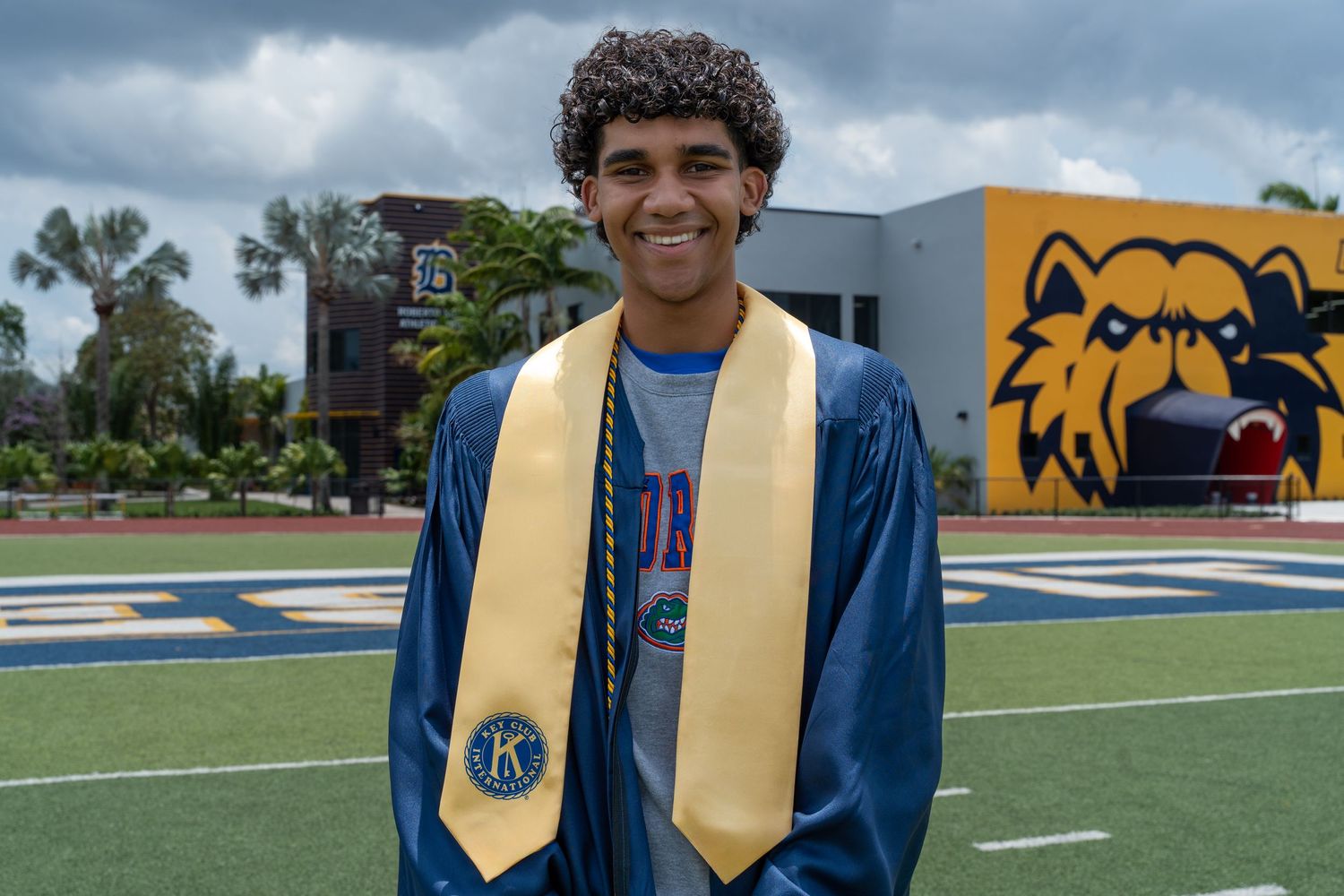 Senior graduate smiles on the football field in a blue and gold cap and stole. Miami senior portraits for graduation.