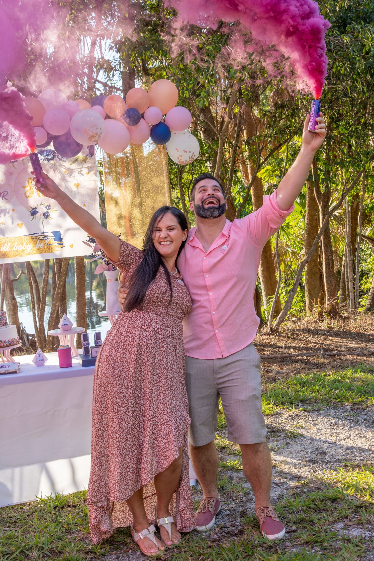 Joyful expecting couple raising their arms as pink smoke reveals the baby’s gender at an outdoor South Florida event.