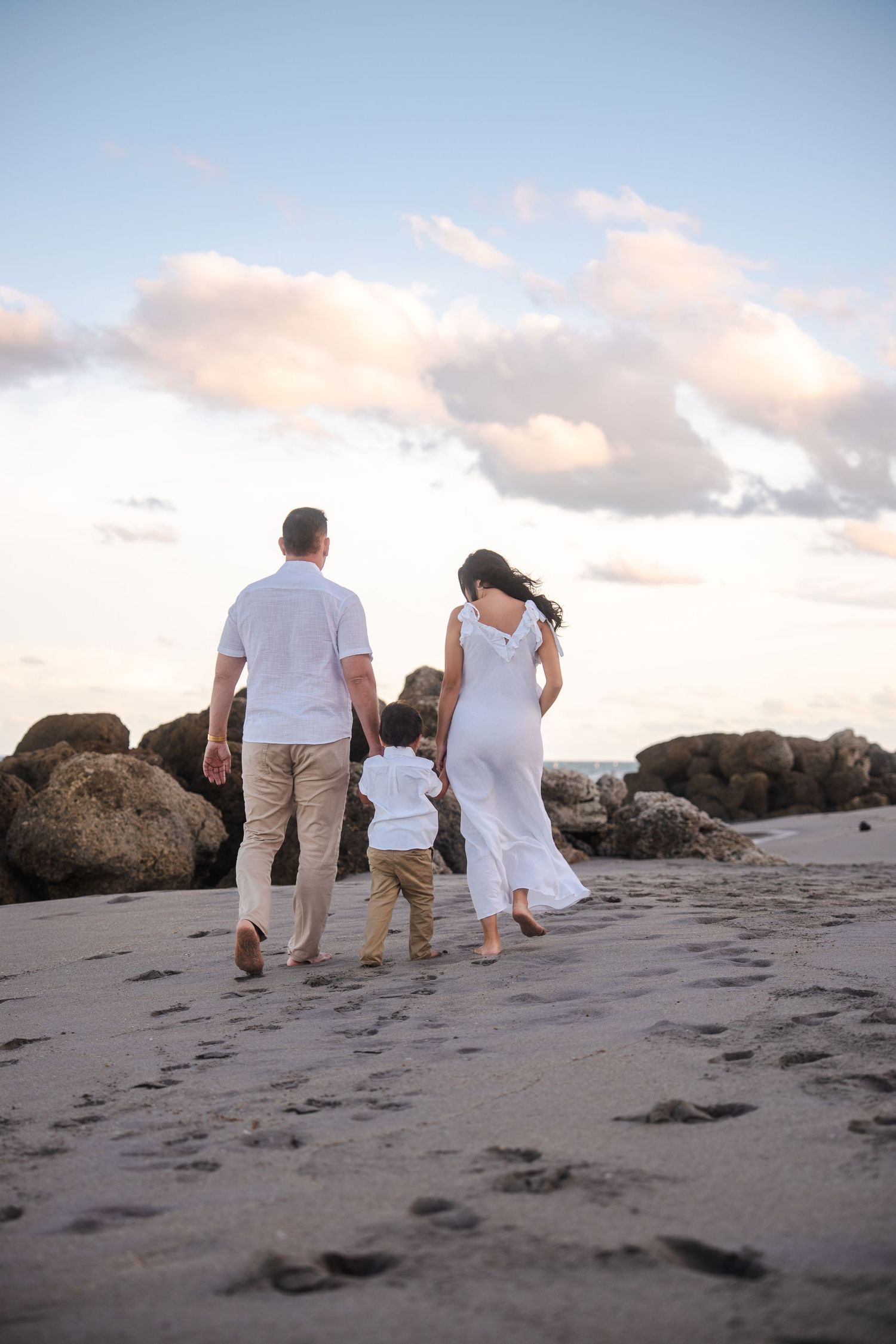 Family walking away from the camera along the shoreline during a pregnancy announcement shoot.