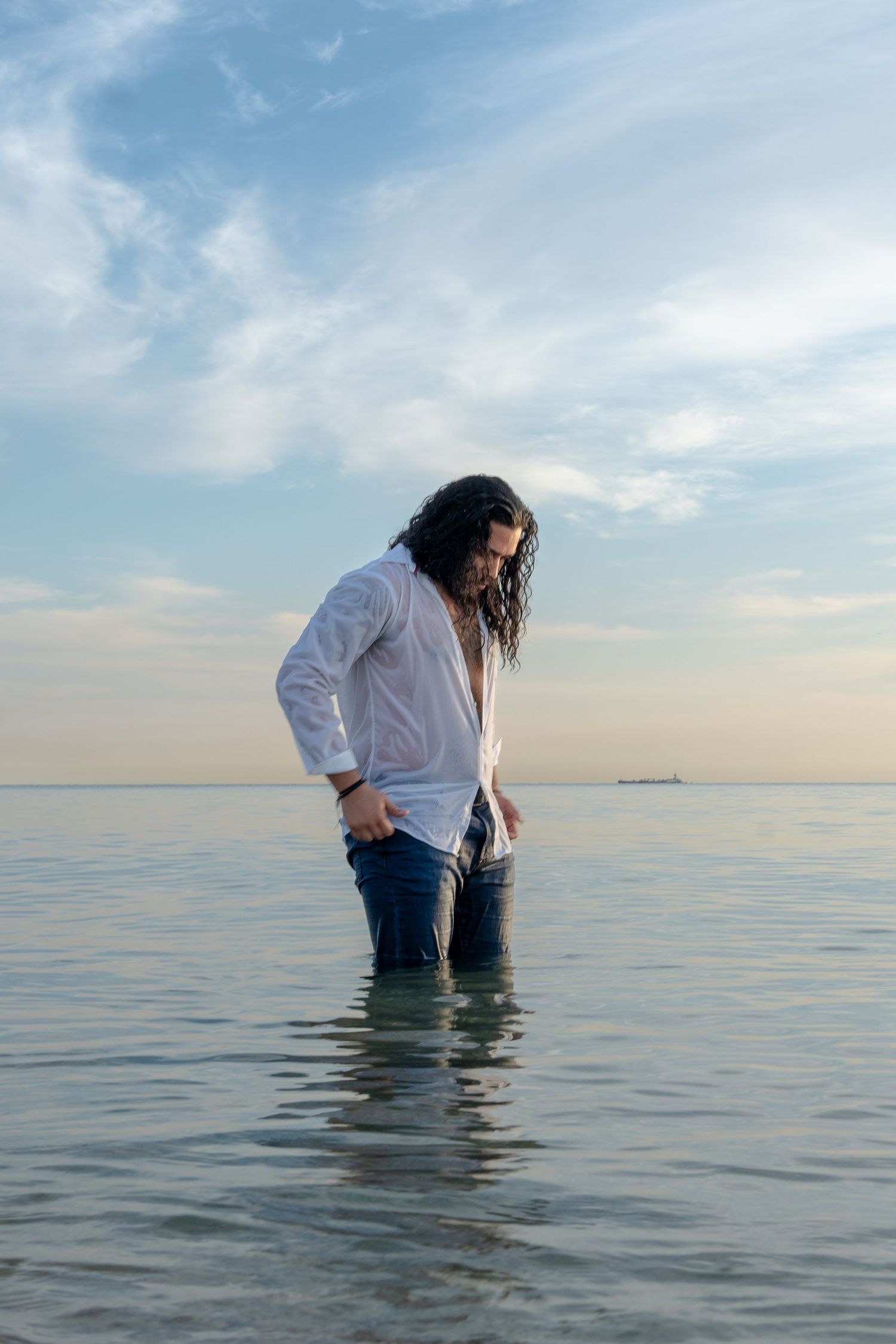 Dreamy beach portrait at sunrise – a male model man in a white shirt stands in the ocean, surrounded by soft pastel skies.