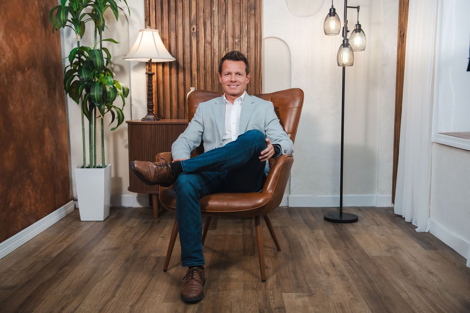A professional sitting in a brown leather armchair in a modern office space with wood paneled walls and warm lighting.