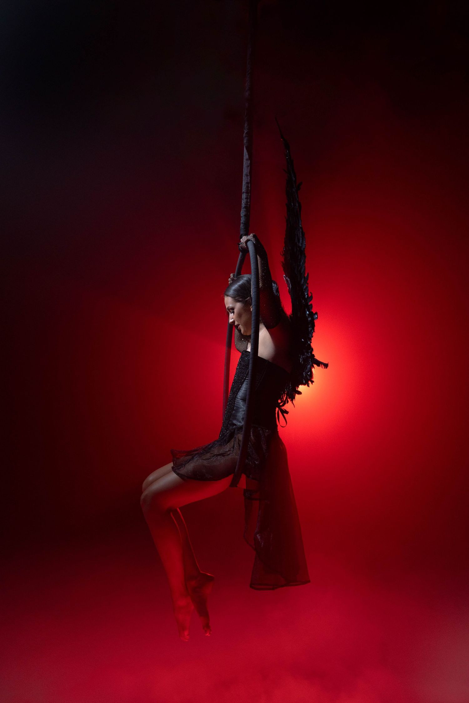 Dark aerial acrobatics at CFX Studio, Miami, FL – gothic-inspired aerialist with wings floating in red mist.