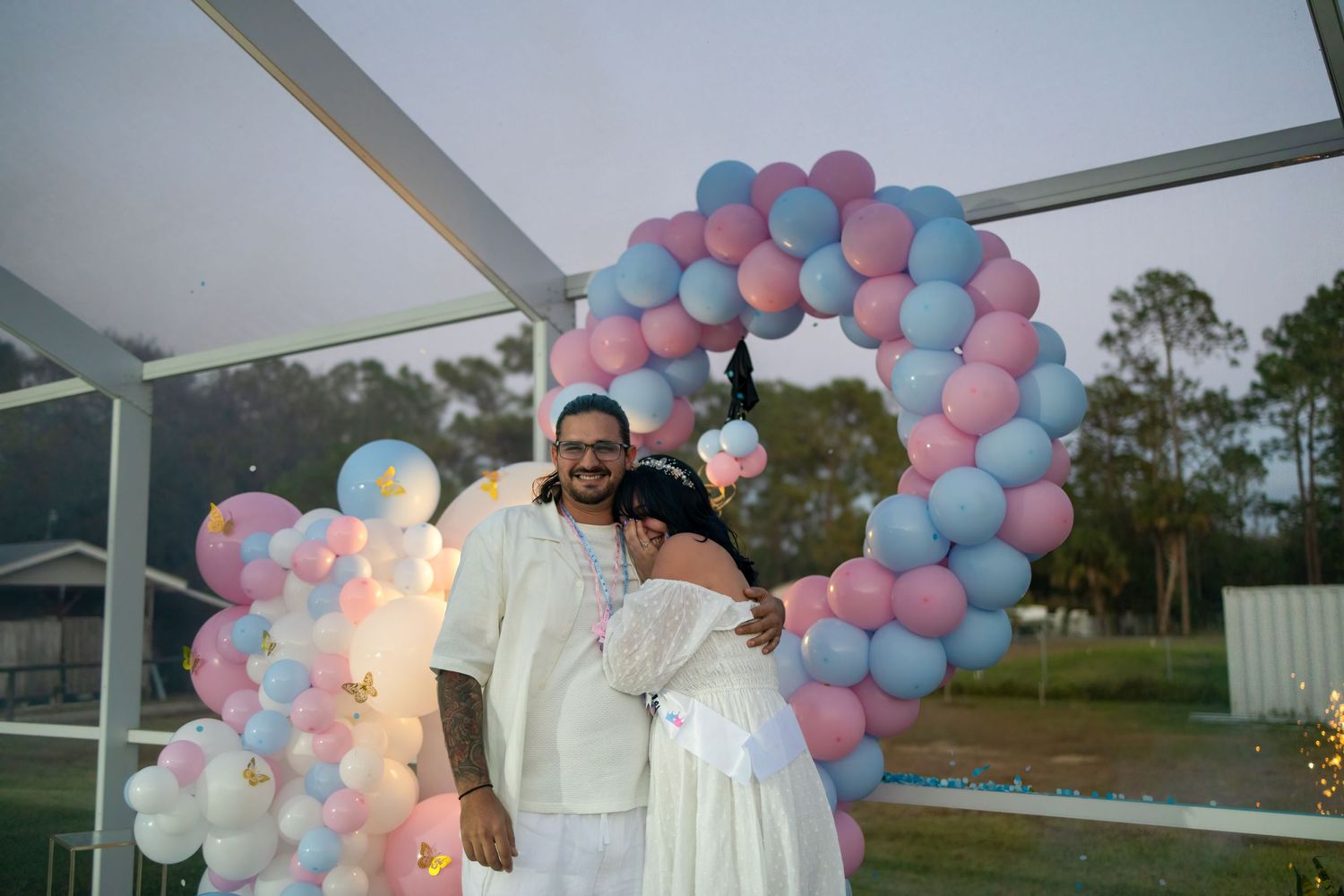 Joyful couple at their gender reveal celebration with pastel balloons, photographed in South Florida.
