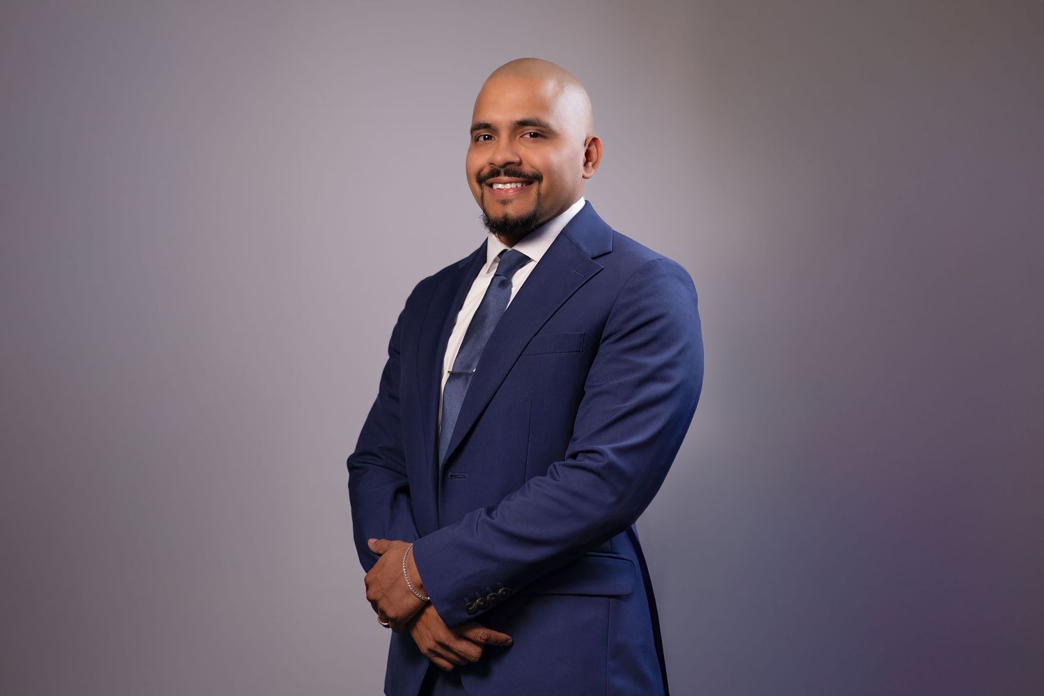 Confident man in a modern blue suit posing with arms crossed in a clean studio setting.