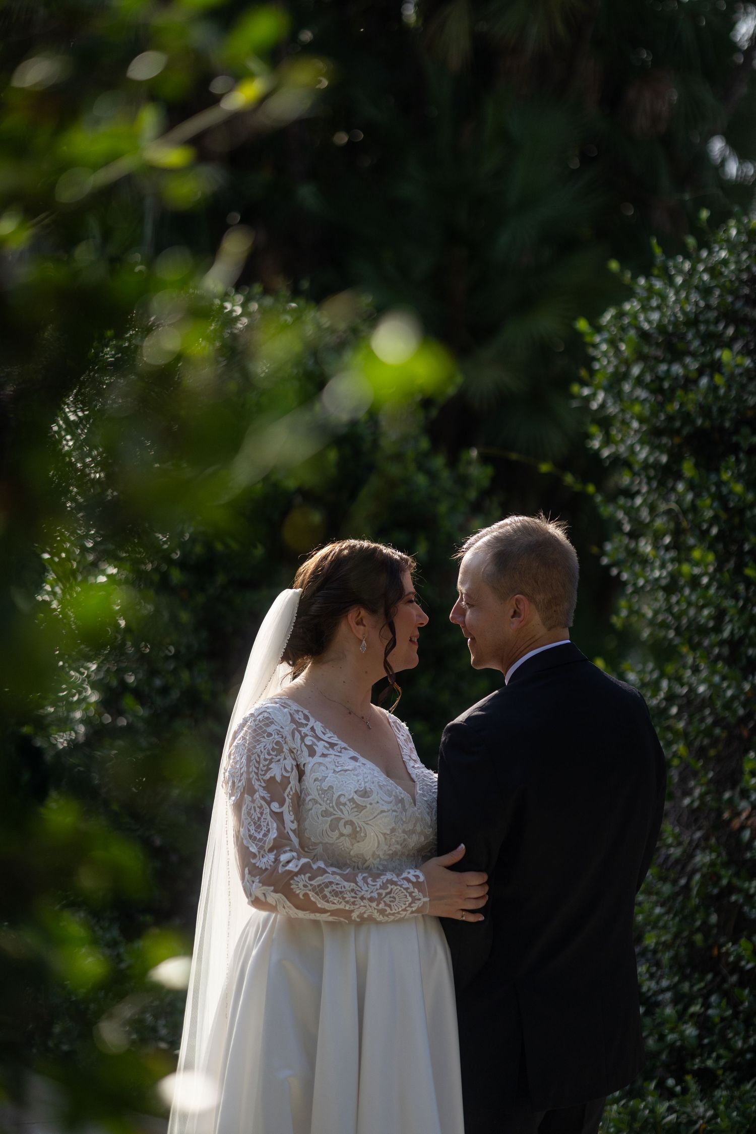 Romantic wedding portrait of a bride and groom standing close in soft natural light, photographed outdoors with a timeless, candid feel.