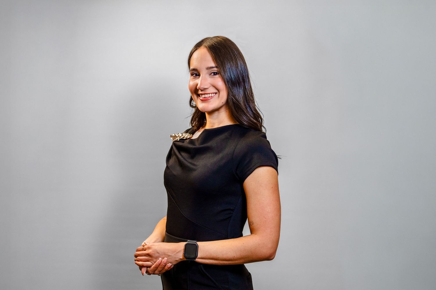 Professional headshot of someone in a black sleeveless top smiling against a gray background.