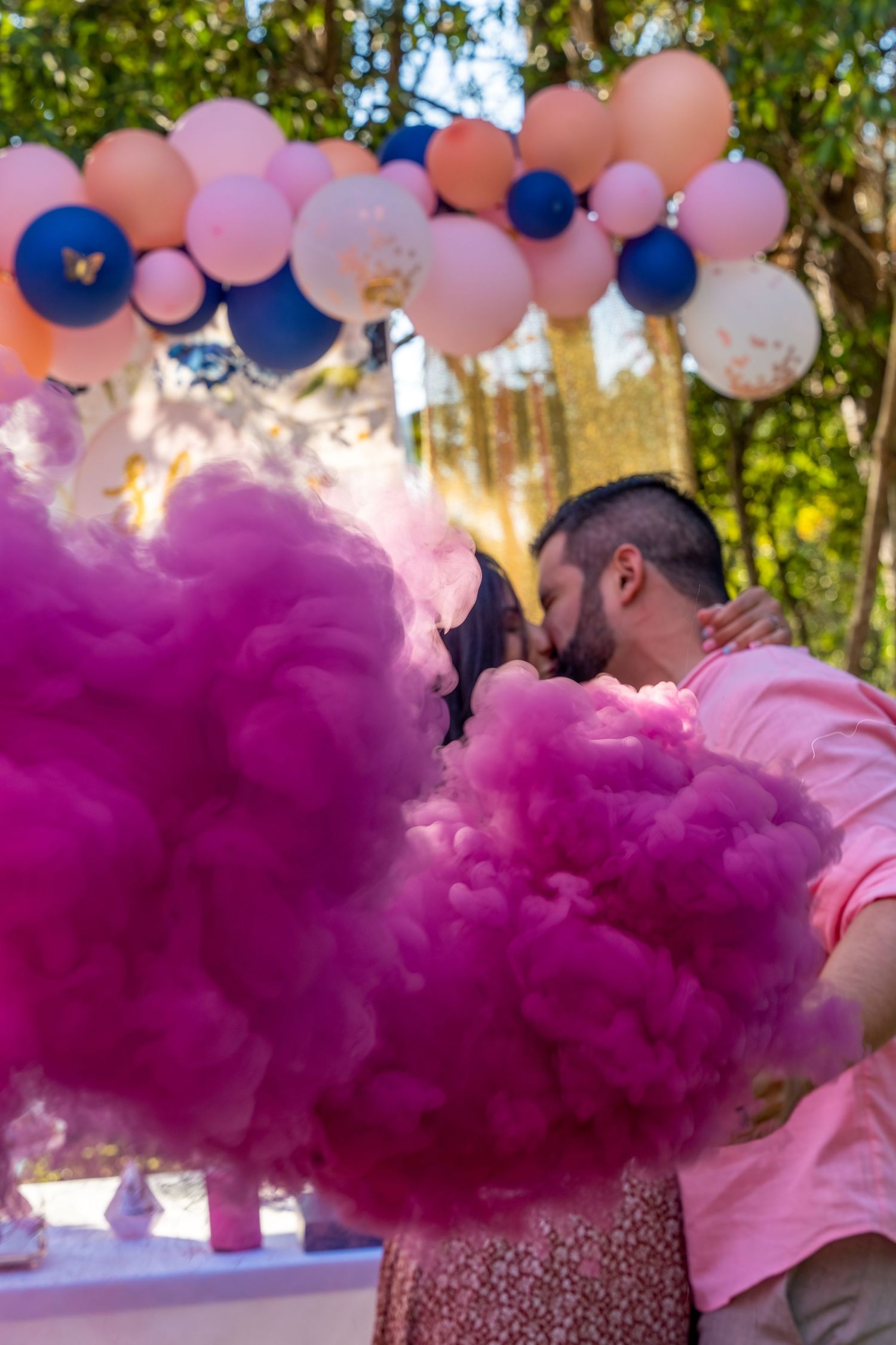 Pink smoke fills the air as an expecting couple celebrates their gender reveal beneath a balloon arch in South Florida