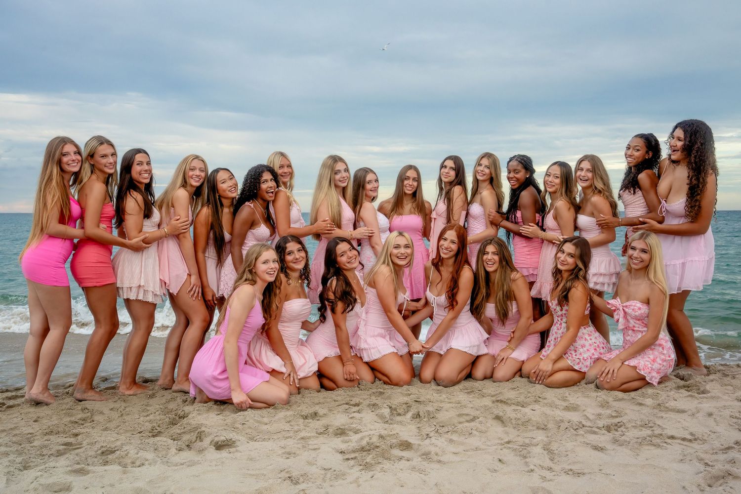 Large cheer squad group photo on the beach, styled in pink outfits and photographed during a South Florida team session.