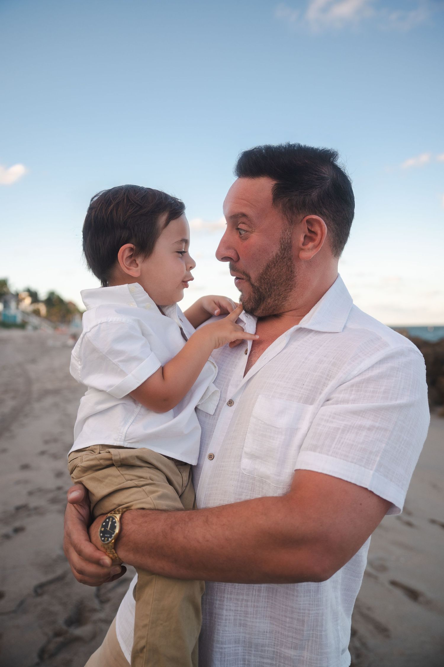 Emotional family pregnancy announcement photo of a father holding his young child on the beach, captured in soft natural light at Deerfield