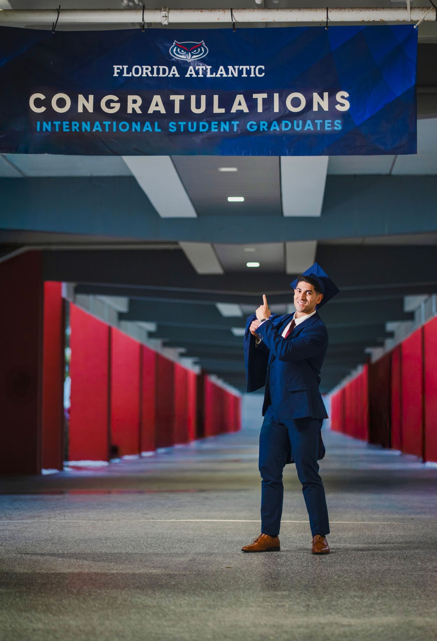 Creative graduation portrait of an FAU graduate standing beneath a campus congratulations sign.