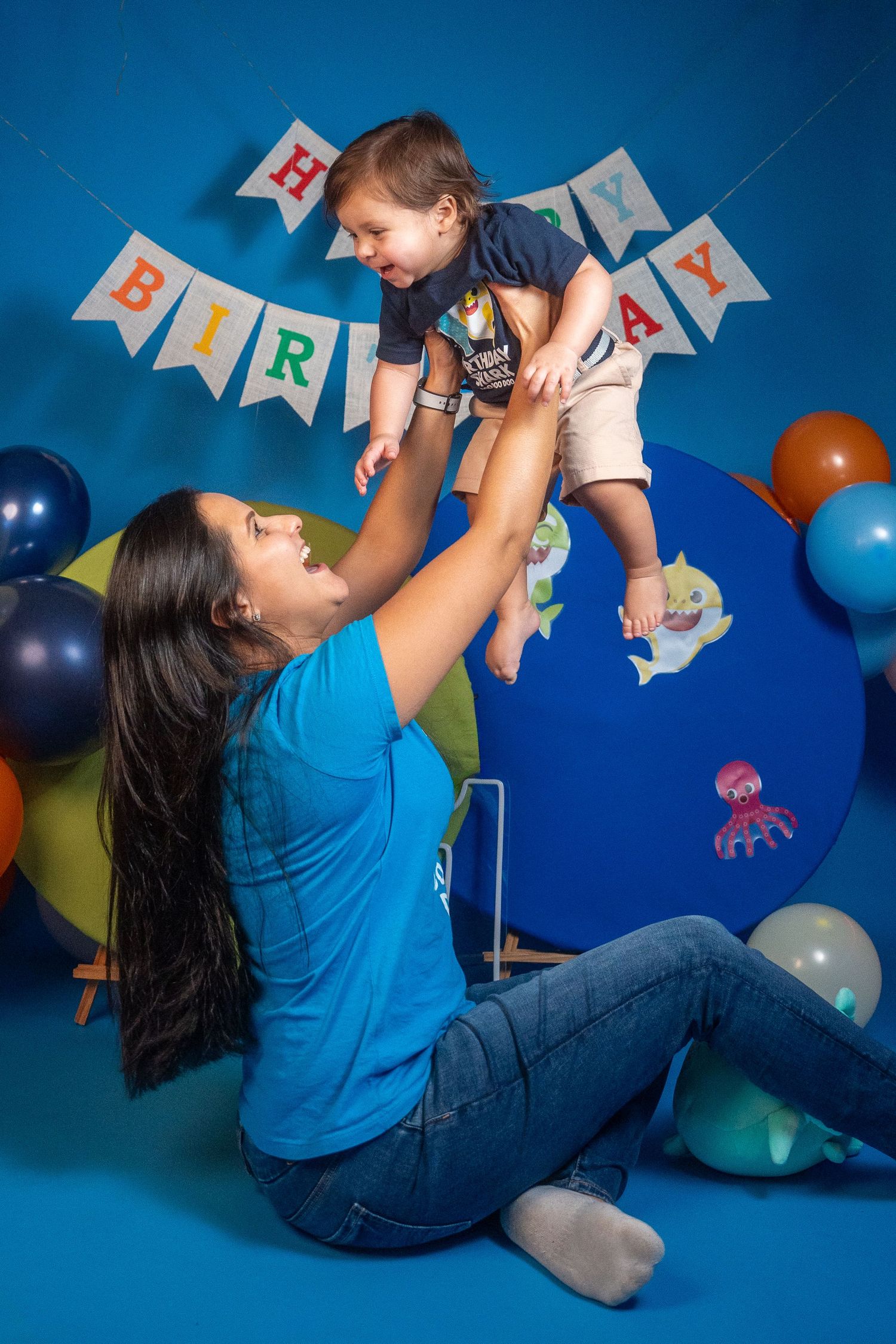 Mother lifting her toddler during a first birthday photo session with balloons and festive decor.