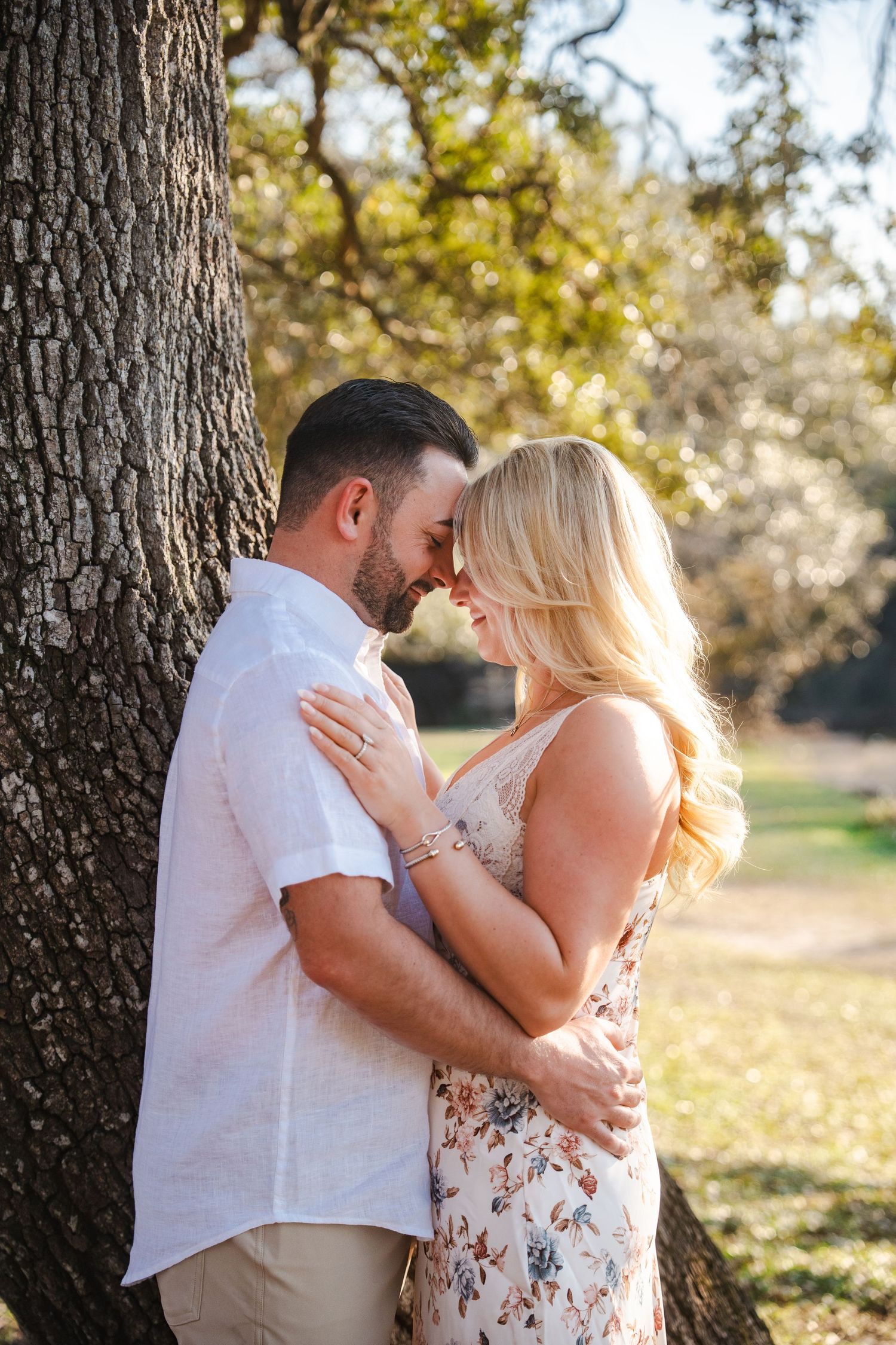 A couple shares an intimate embrace in a sun-dappled orchard during a romantic outdoor photoshoot.