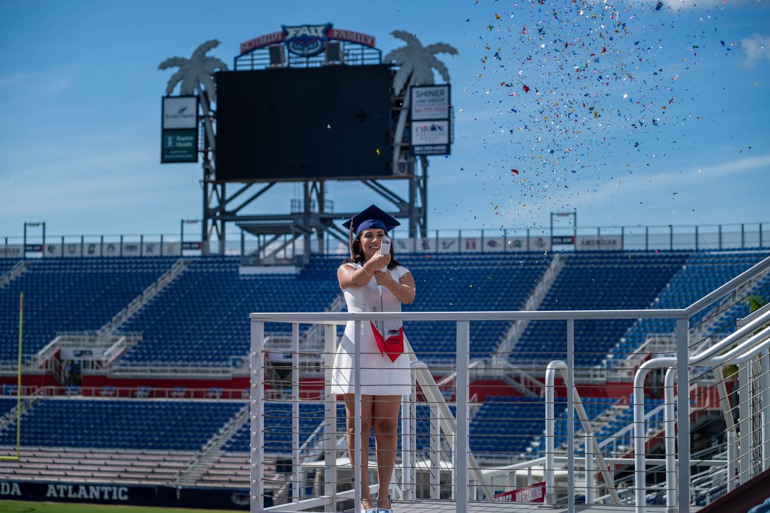 FAU graduation photography of student celebrating with cap and gown in stadium