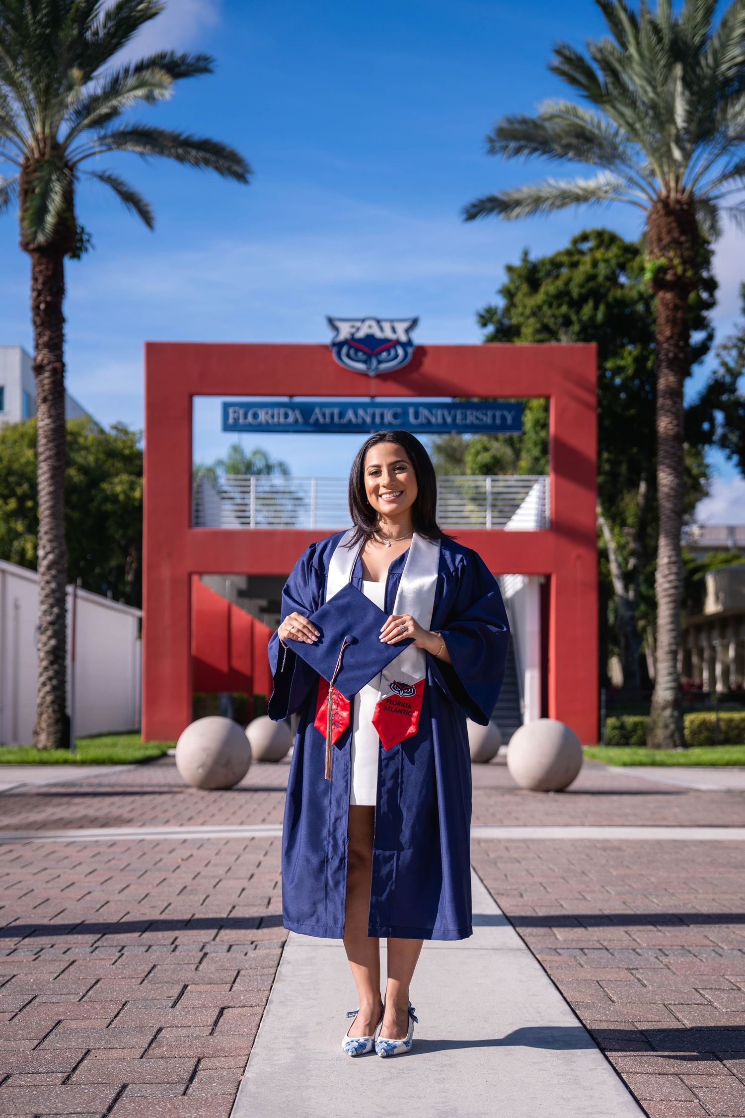 FAU student in graduation gown standing at campus entrance with red arch